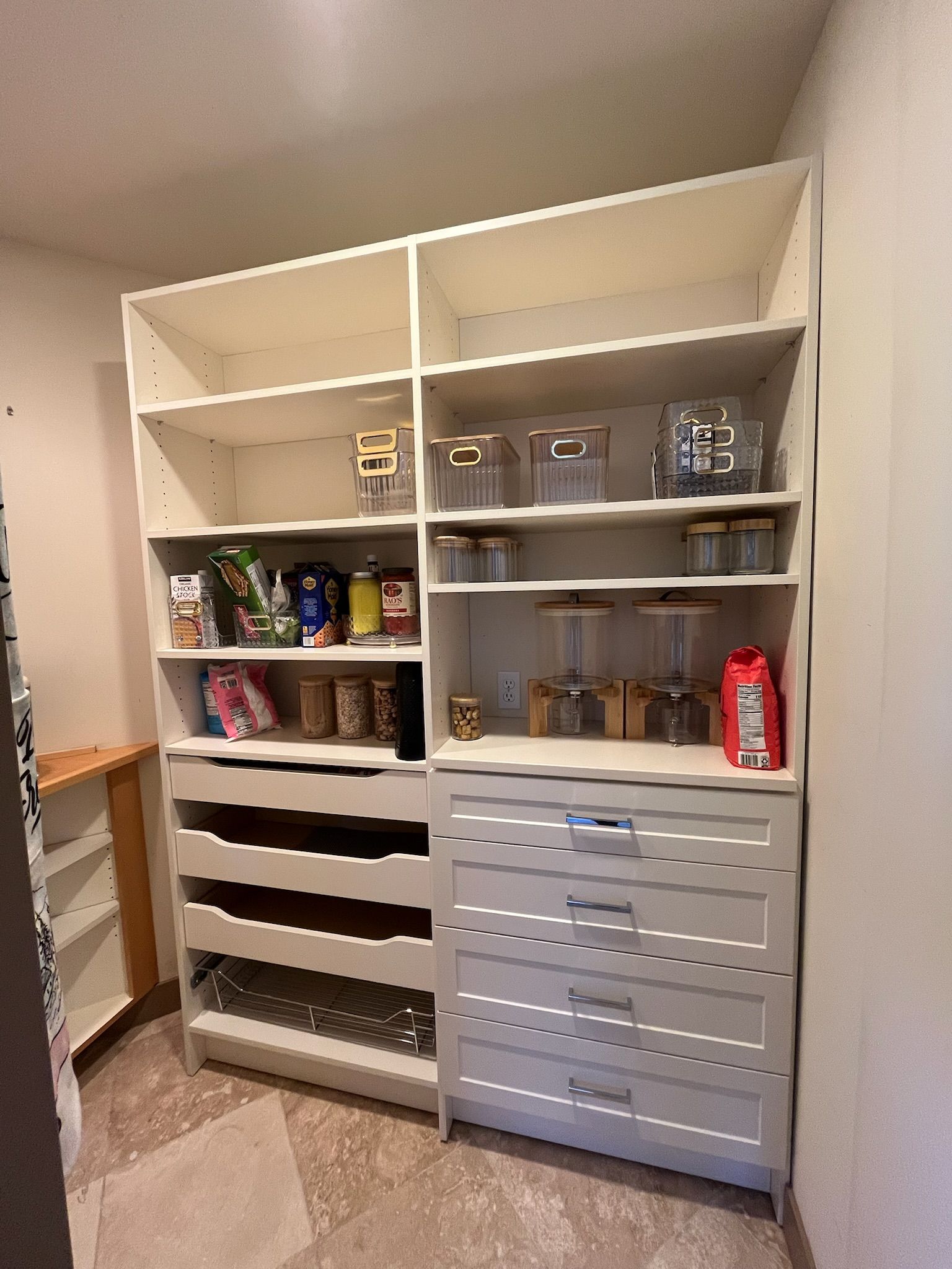 Built-in white pantry shelving with bins, canned goods, and drawers in a home closet-like storage room