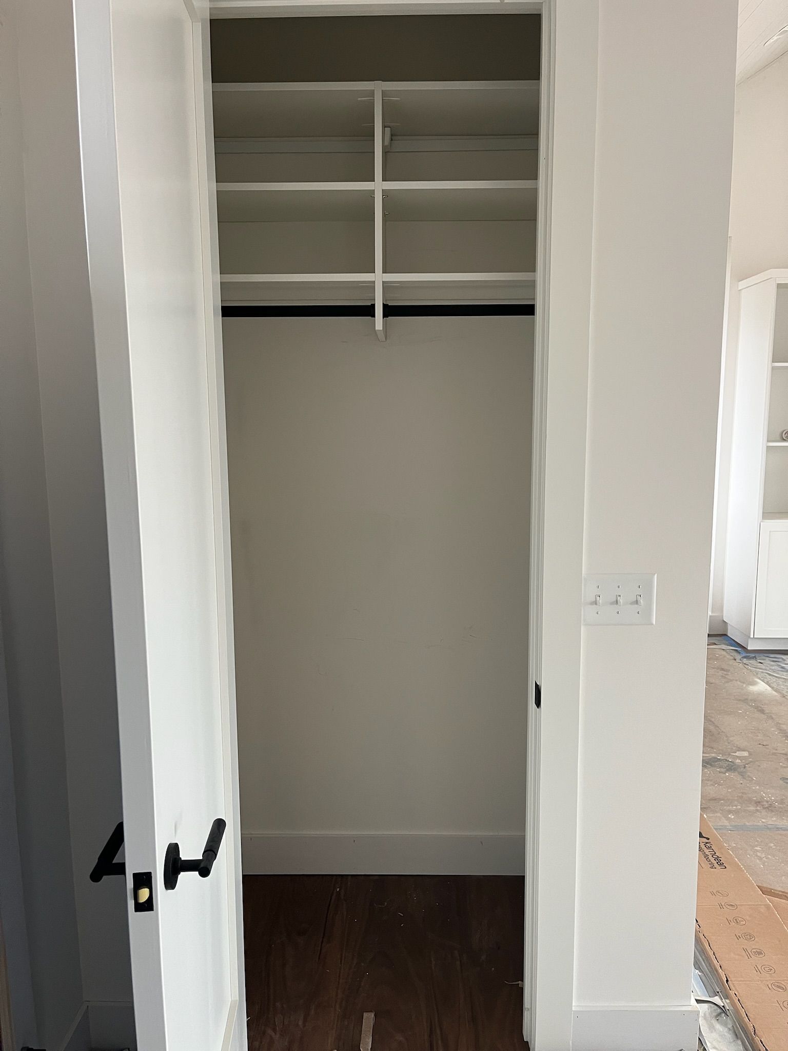Open closet with white shelves and hanging rod, dark wood floor, and white doors.