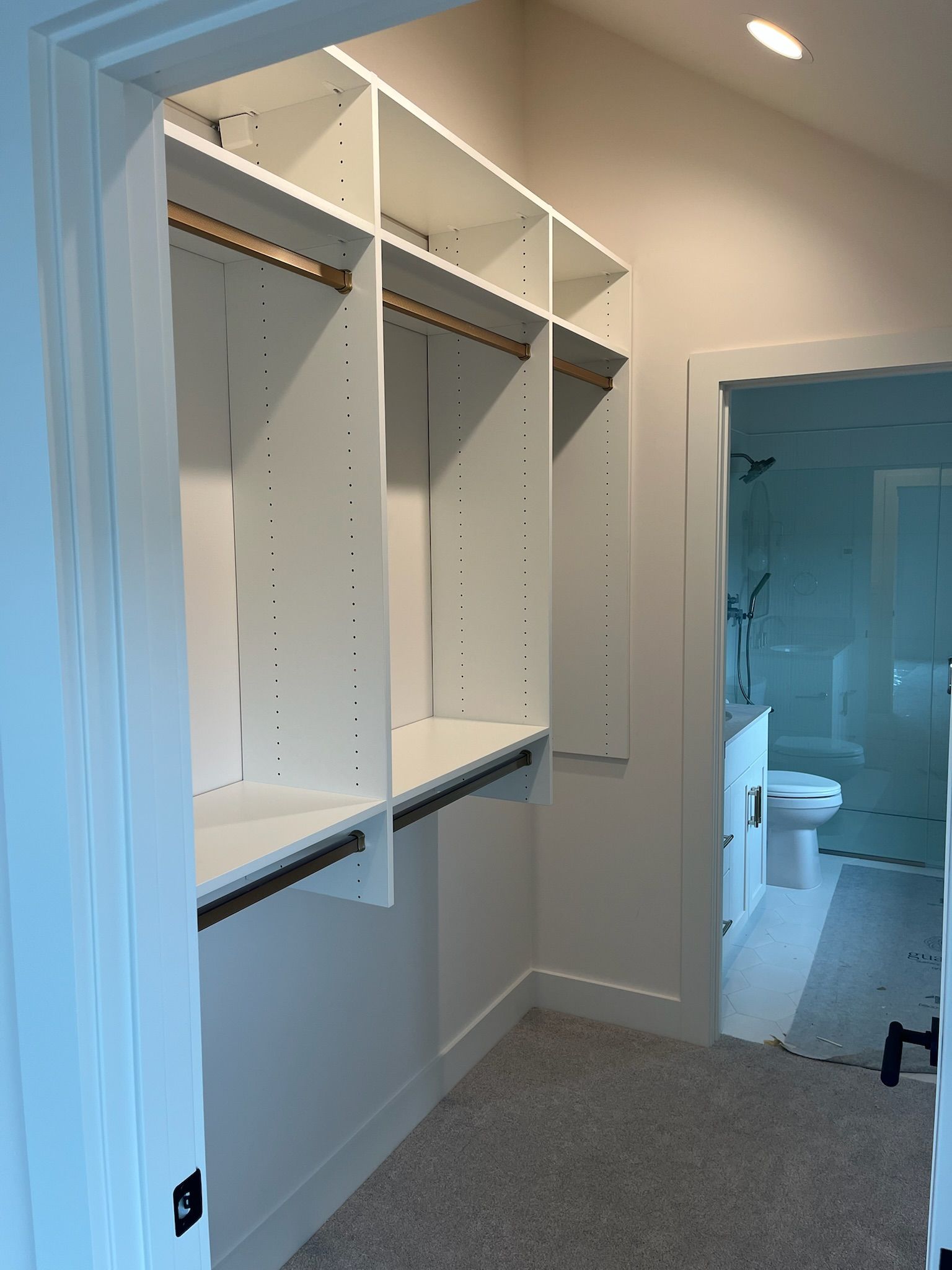 Empty walk-in closet with white shelving and hanging rods beside a bathroom doorway.