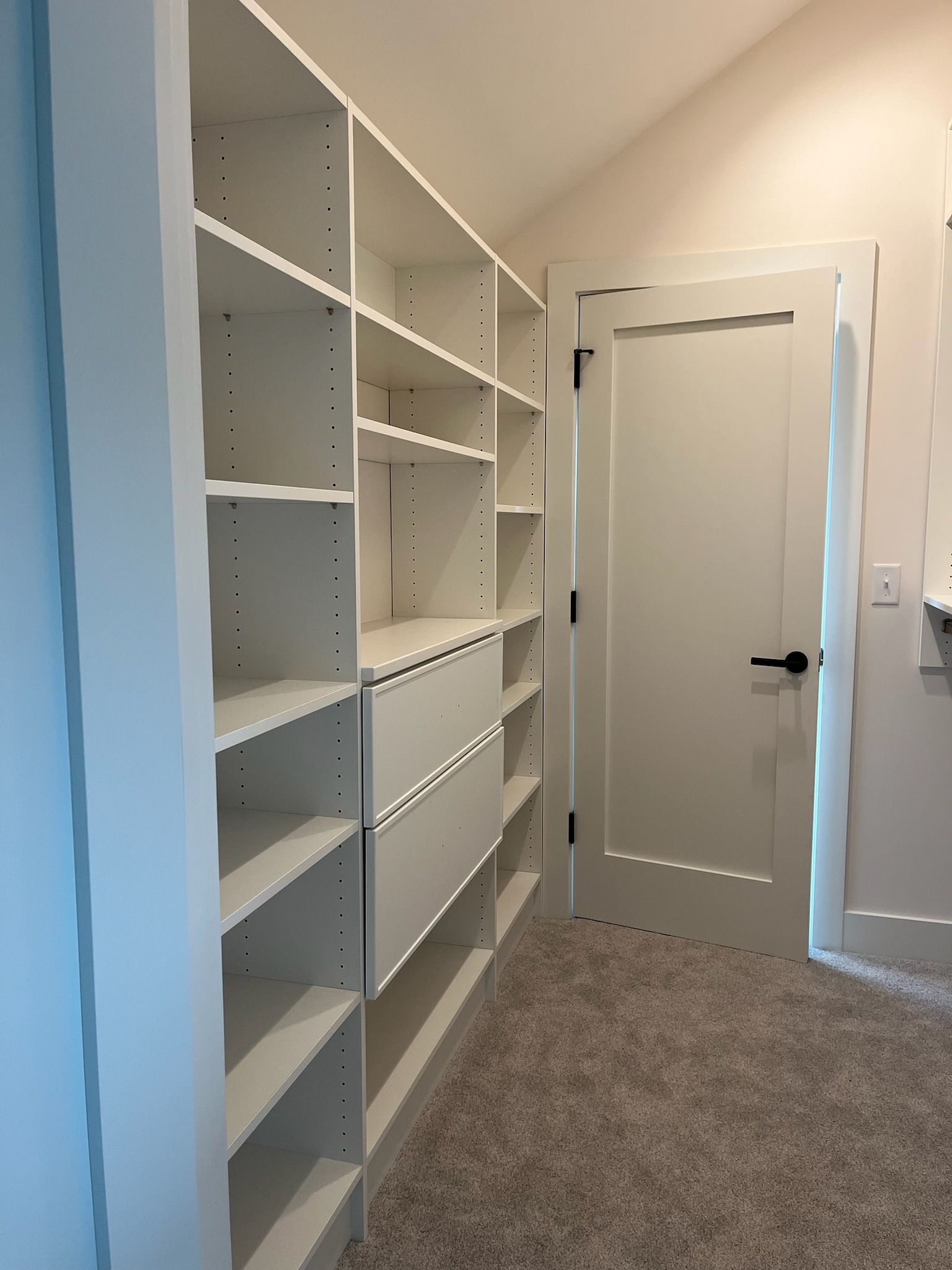 Narrow hallway with white built-in shelves and drawers along the left wall and a closed white door at the end.