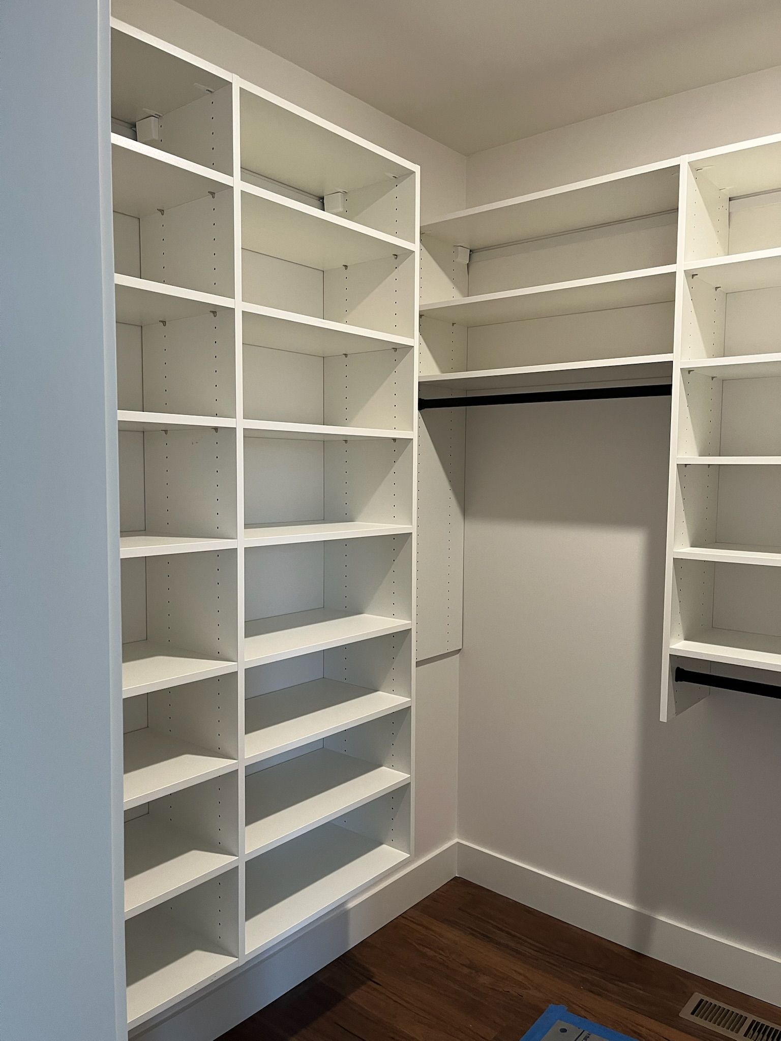 Empty walk-in closet with white built-in shelves and hanging rods over a dark wood floor.