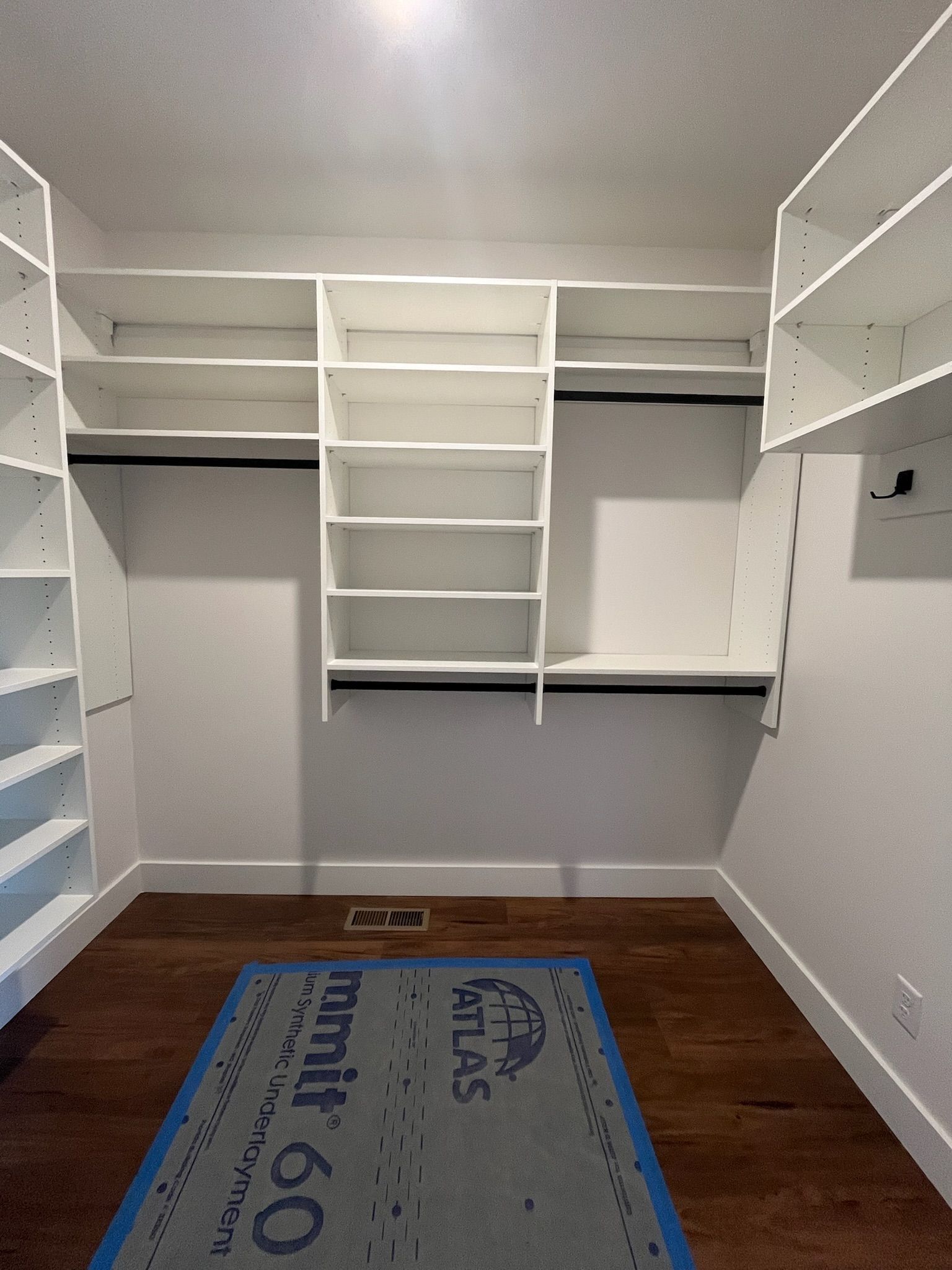 Empty white walk-in closet with built-in shelves and hanging rods, gray walls, and a brown floor.