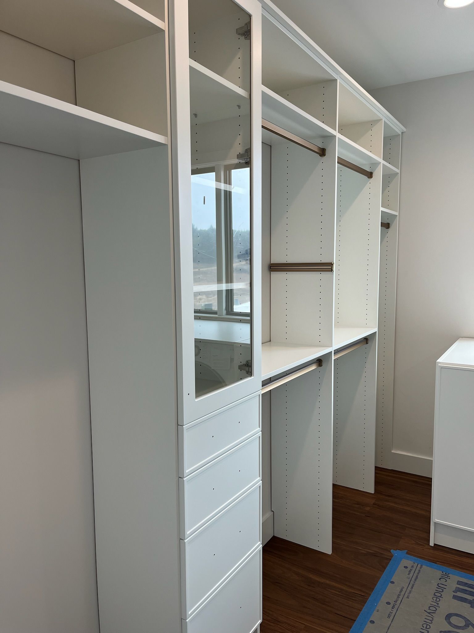 White built-in closet system with shelves, drawers, and a mirrored cabinet in a modern room.