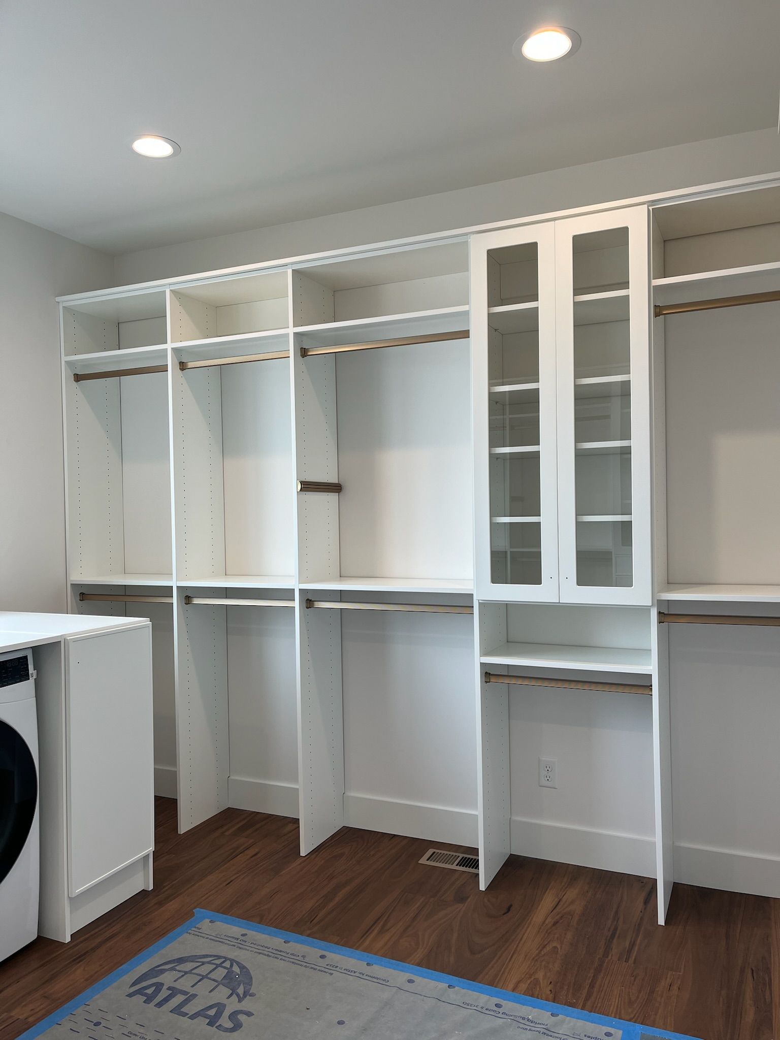 White built-in closet shelves and cabinets in a laundry room with a washer on the left.