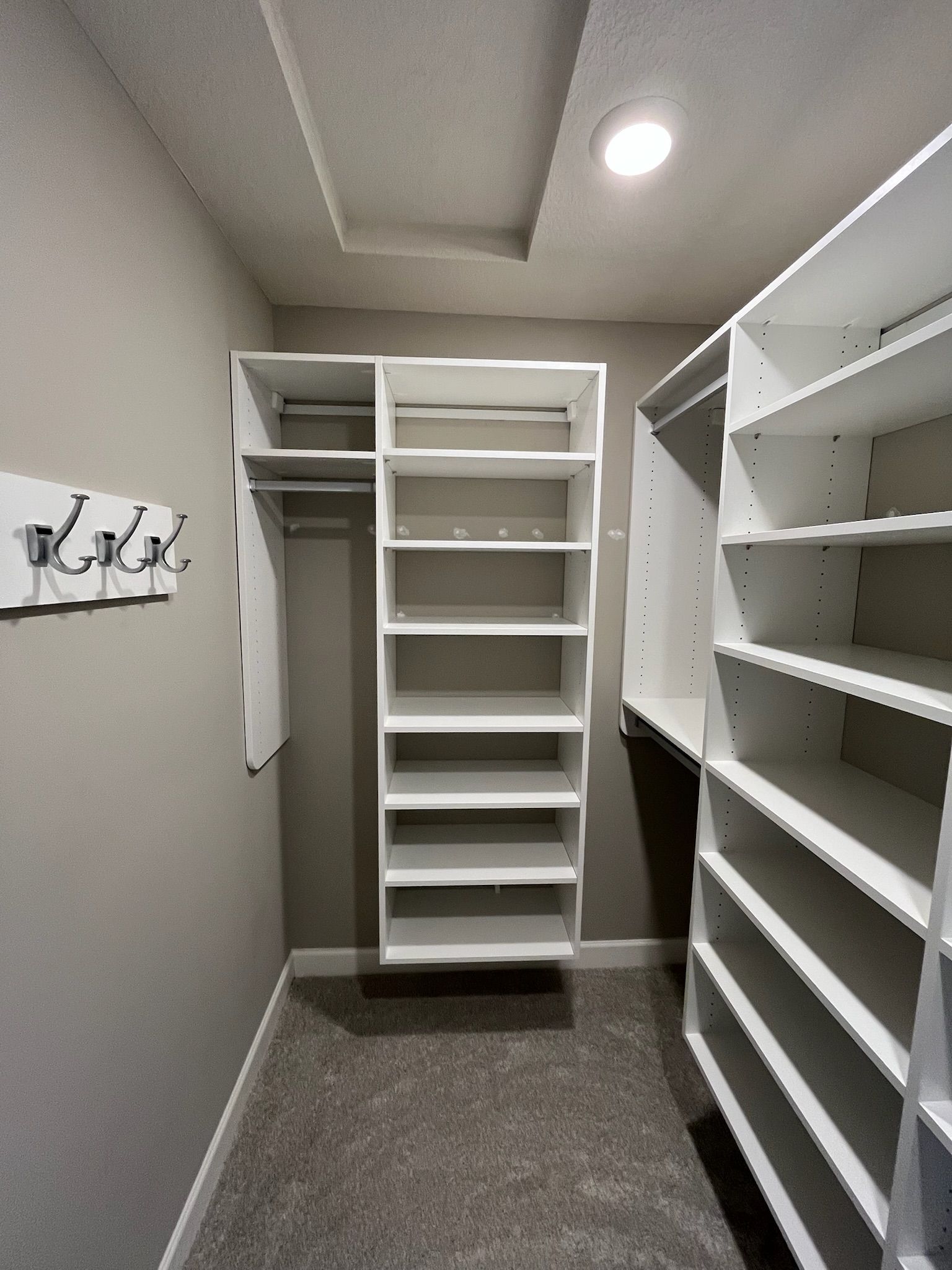 Walk-in closet with white built-in shelves, hanging rods, and a gray carpeted floor.