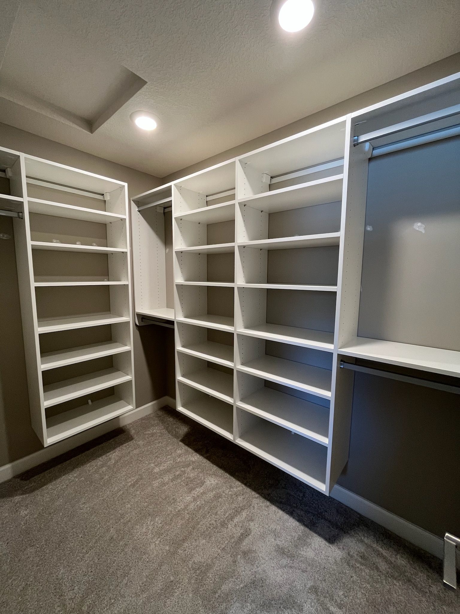 Empty walk-in closet with white shelving, gray carpet, and a window on the right.