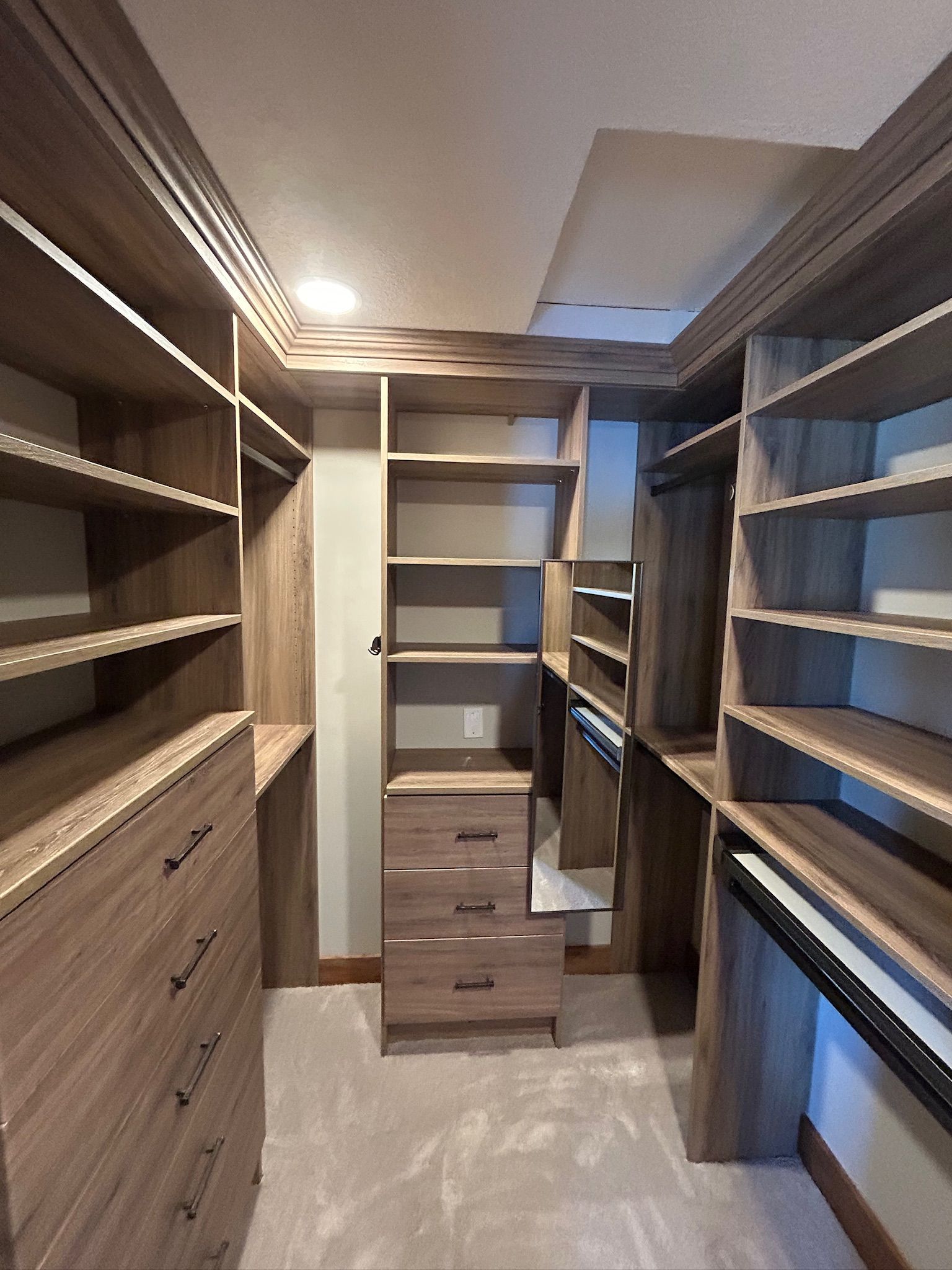 Walk-in closet with wooden shelves, drawers, and a skylight ceiling in a narrow hallway-like space