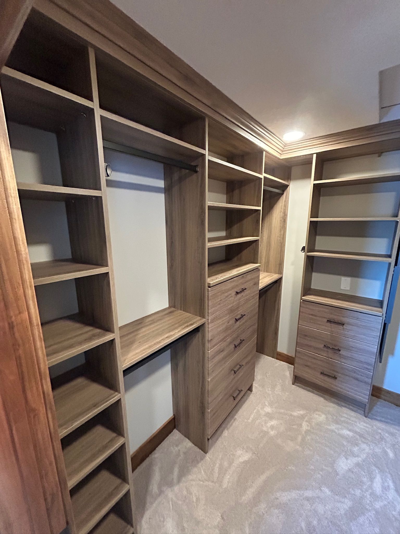 Built-in wooden walk-in closet with shelves, drawers, hanging spaces, and a central mirror.
