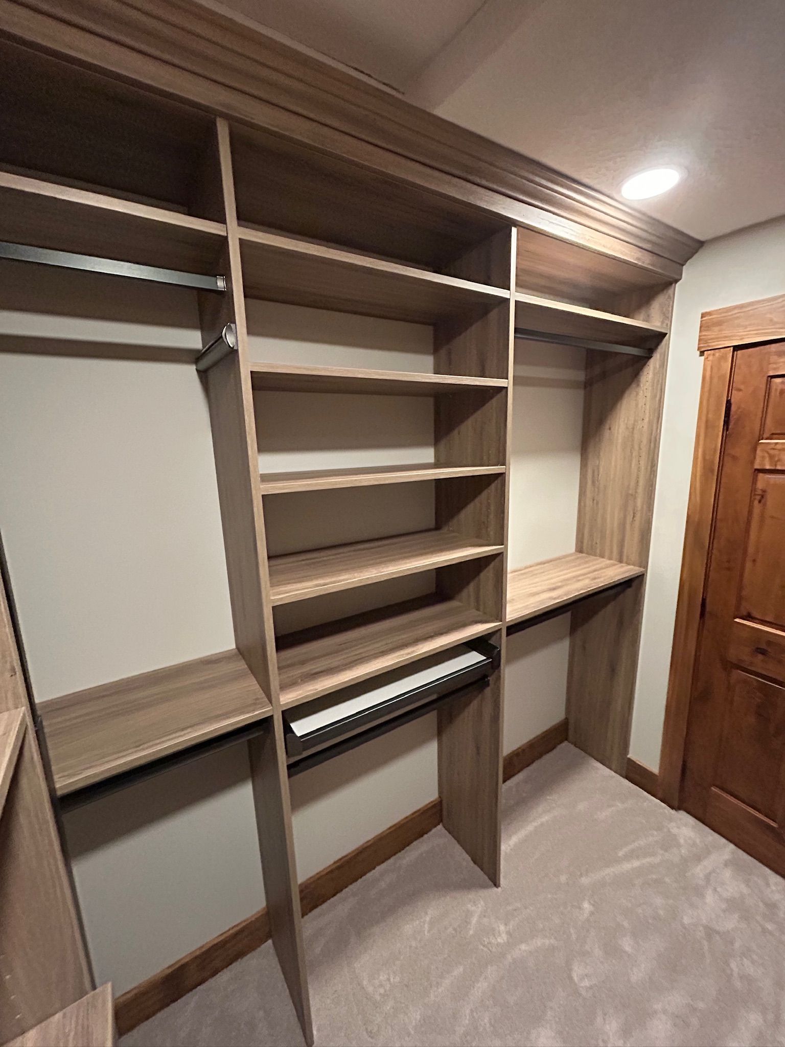 Built-in closet with gray shelves, hanging rods, and beige carpet in a walk-in room