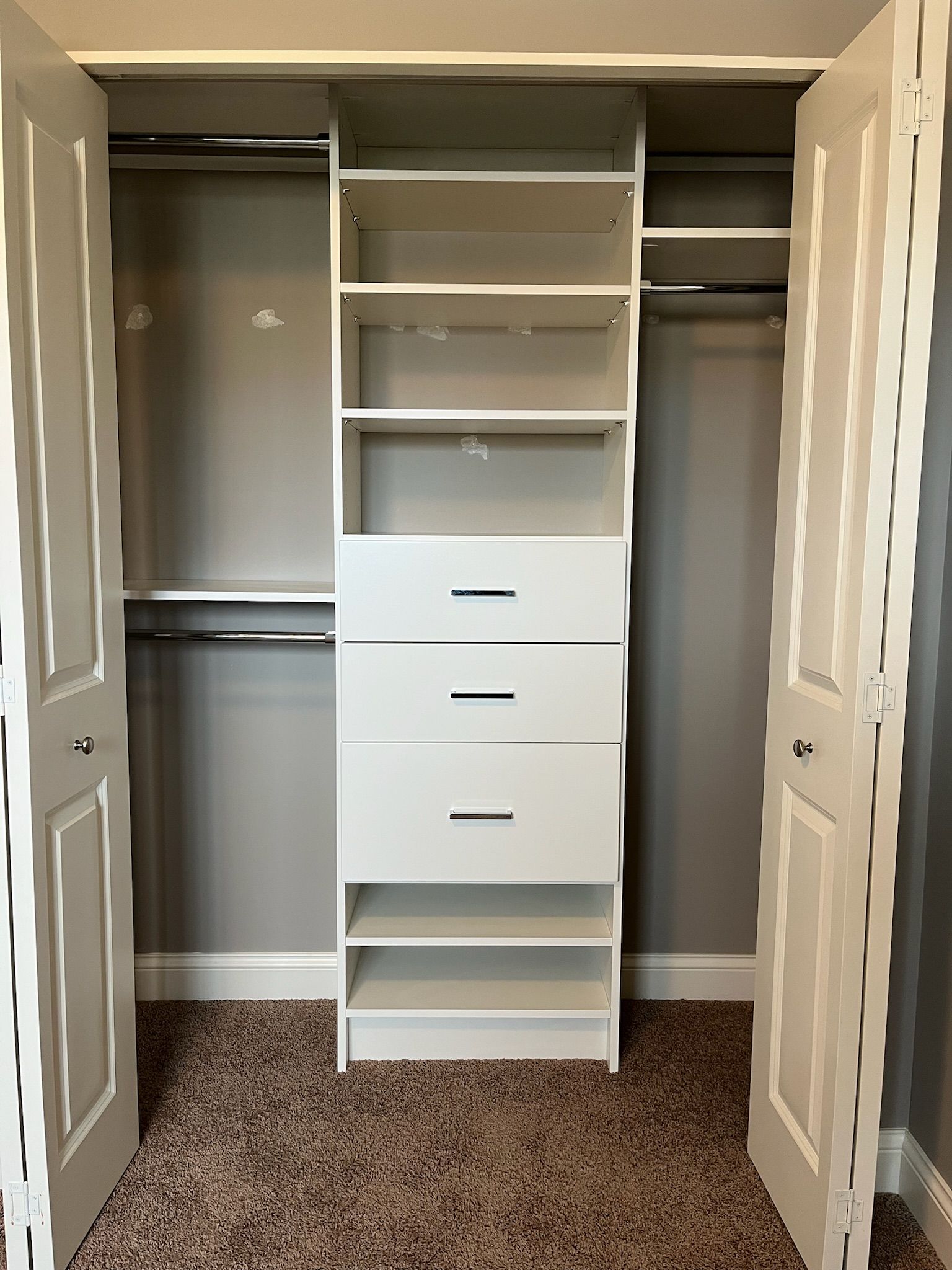 Open closet with white built-in shelves and drawers, beige carpet, and folding doors.