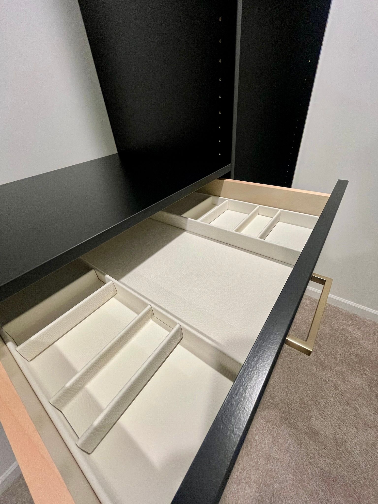 Empty open drawer organizer with white fabric bins and a beige tray in a black-and-white cabinet.