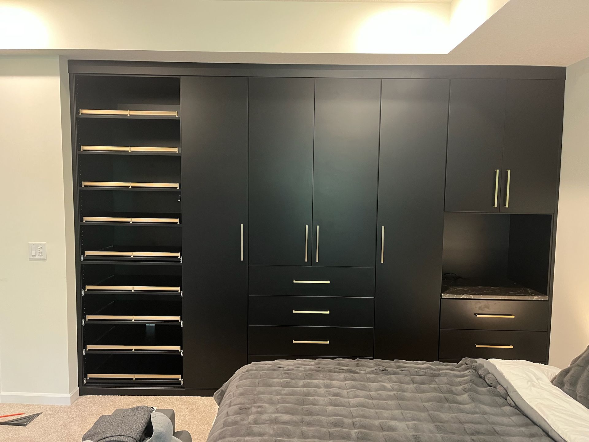 Black built-in wardrobe and shelving wall in a bedroom with a gray bed in the foreground.