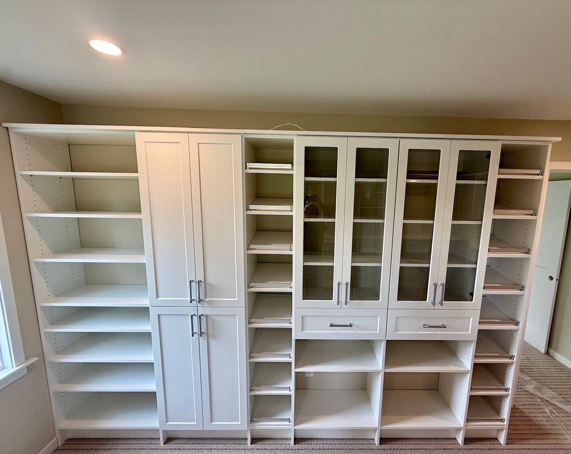 White built-in cabinets with shelves and glass-front doors along a wall in a room.