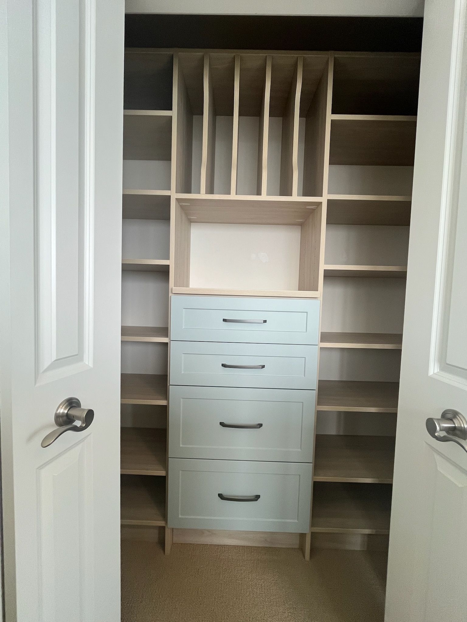 Open closet with built-in shelves and a blue drawer unit centered between white doors.