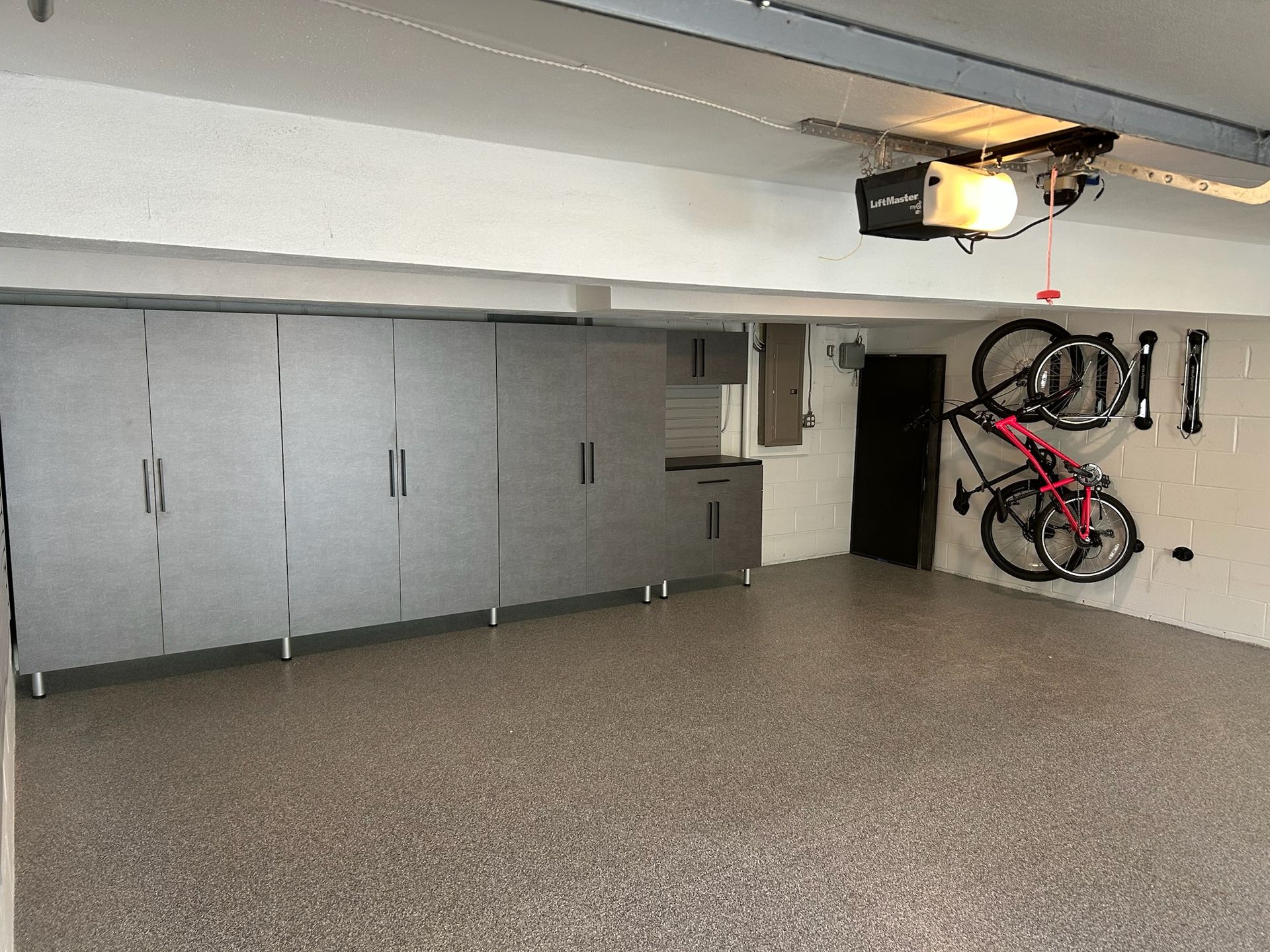 Two bicycles hanging in a tidy garage with gray storage cabinets and a speckled floor.