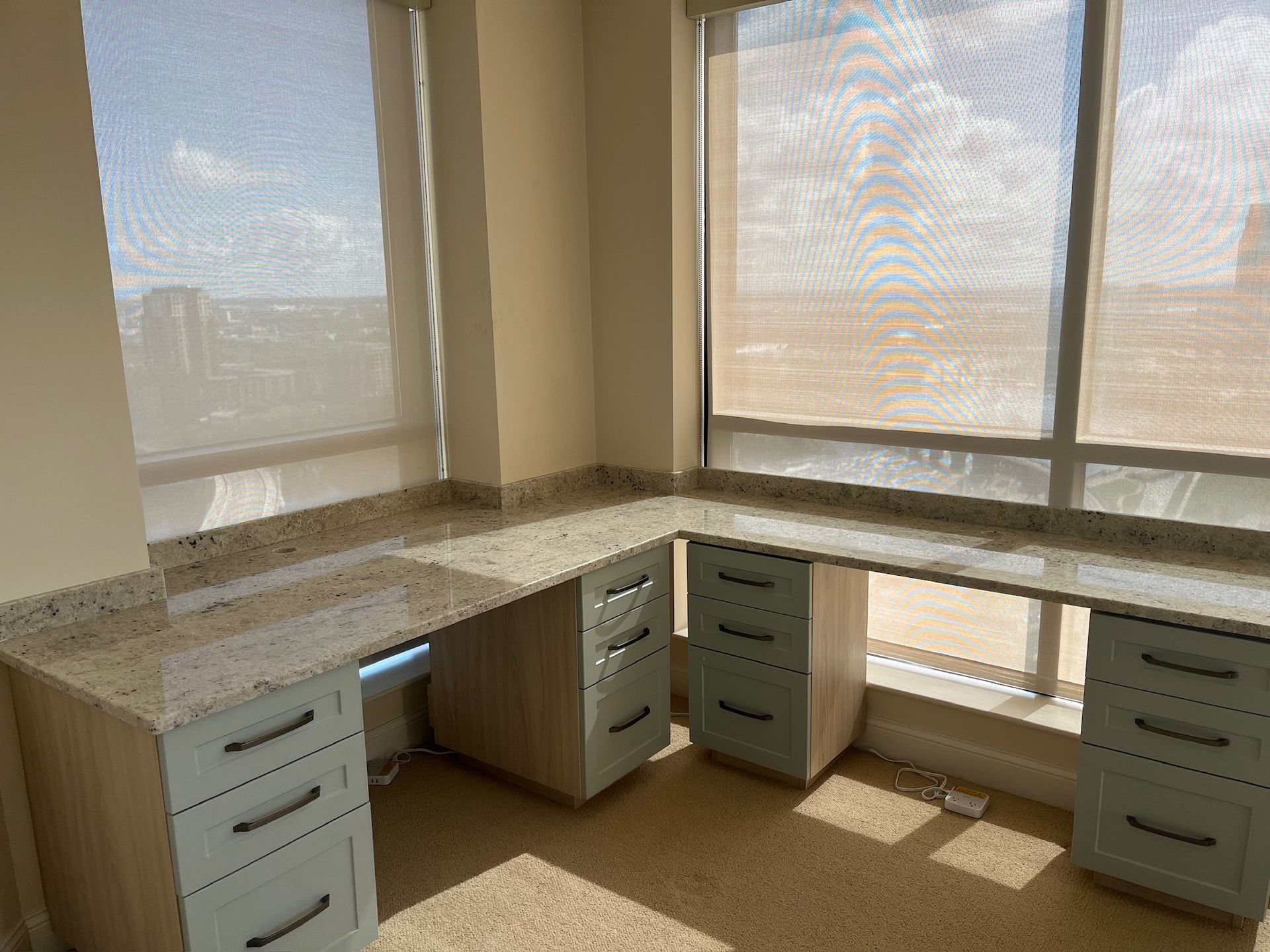 Corner office desk setup with beige cabinets and granite top by large sunlit windows