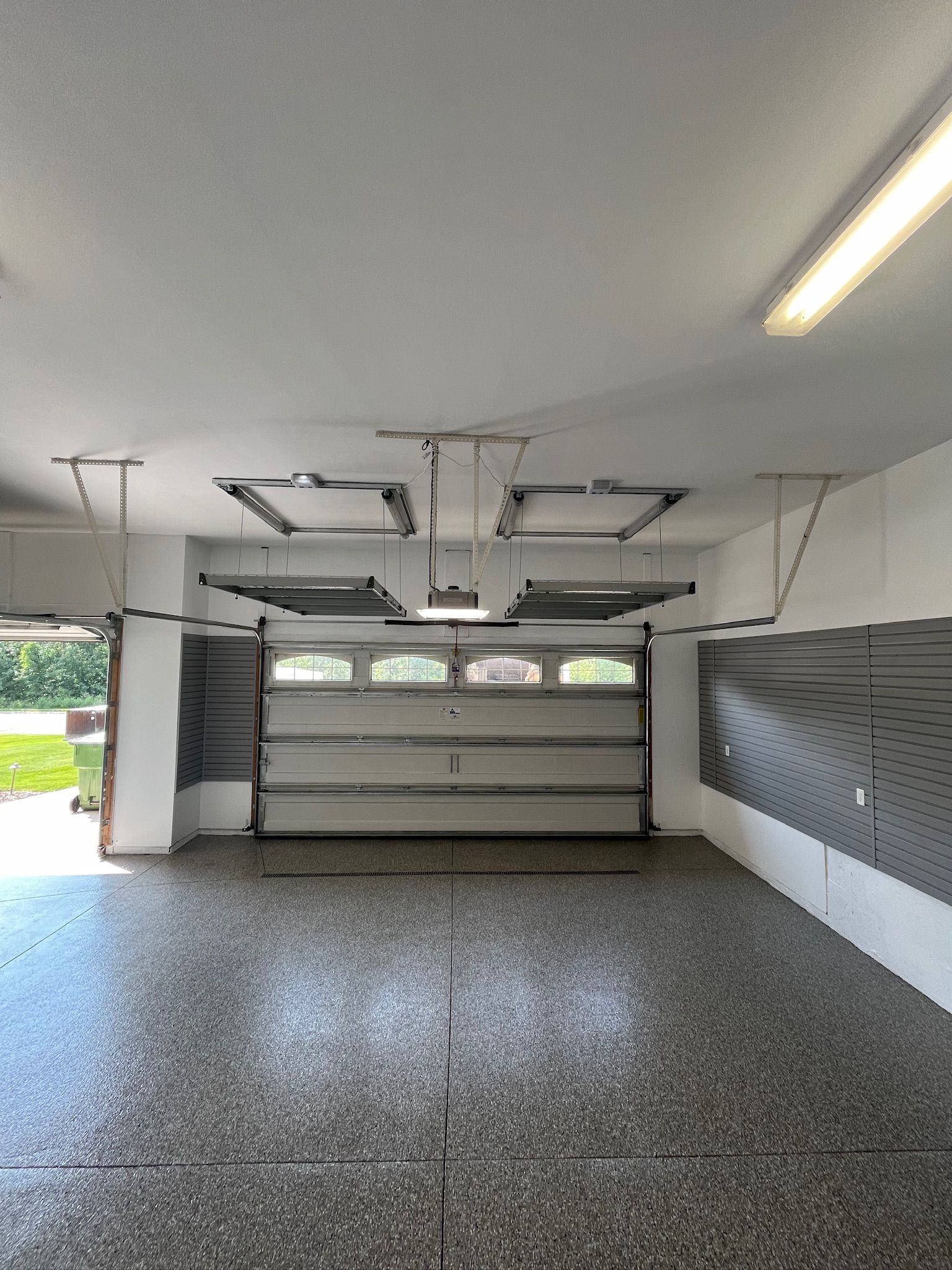 Empty garage interior with open sectional door, gray speckled floor, and ceiling lights