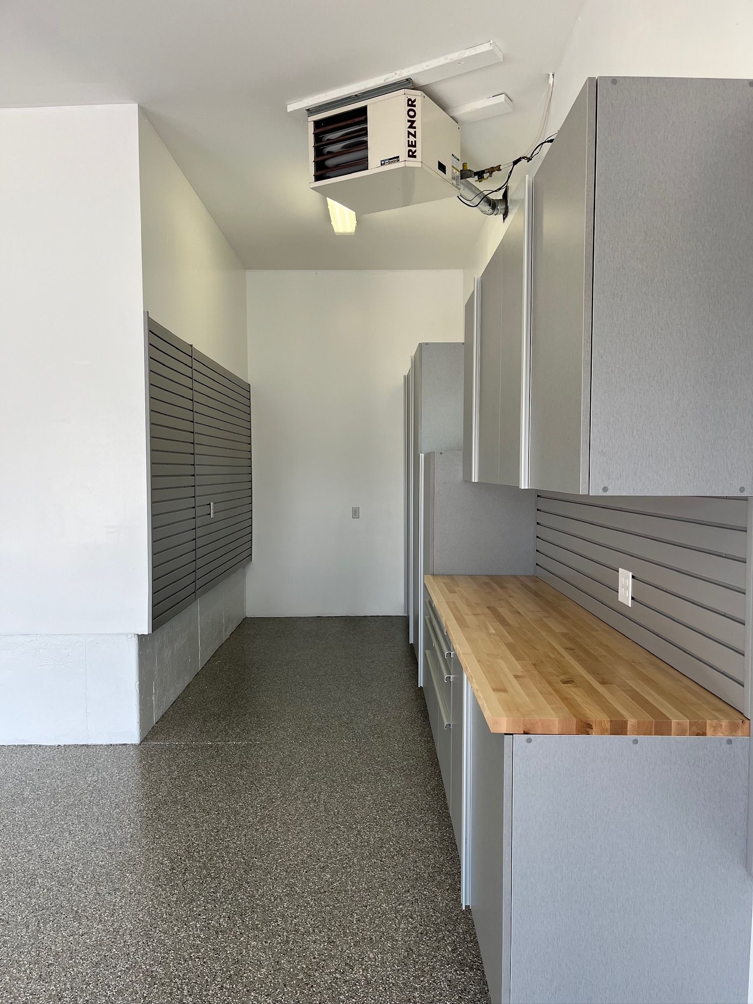 Garage with gray storage cabinets, wooden workbench, pegboard wall, and ceiling-mounted heater.