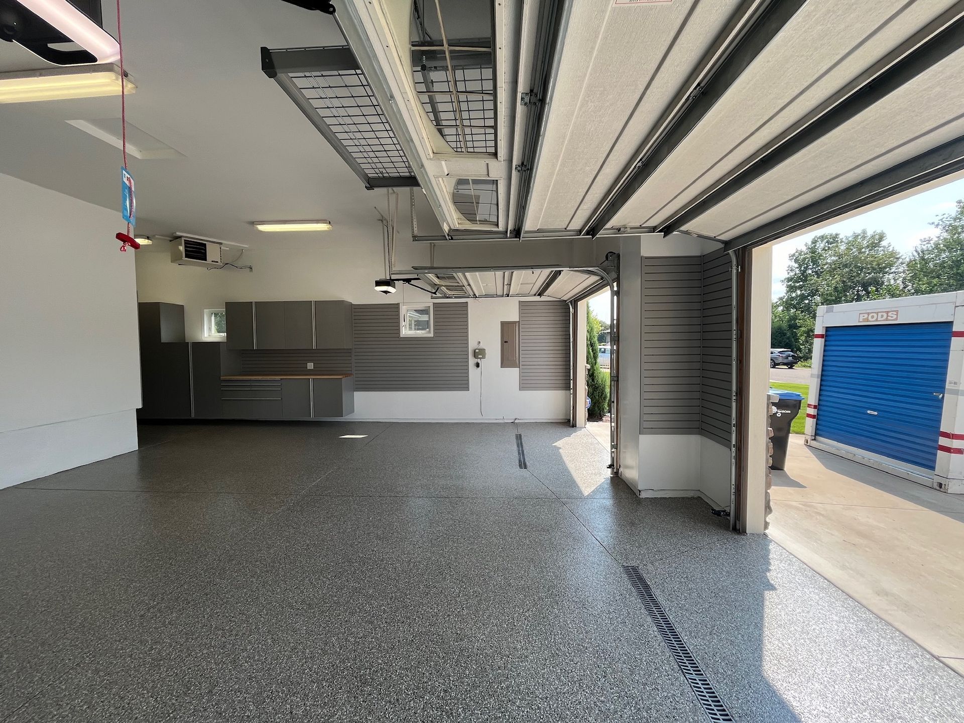 Empty garage interior with speckled floor, open door, and blue dumpster outside