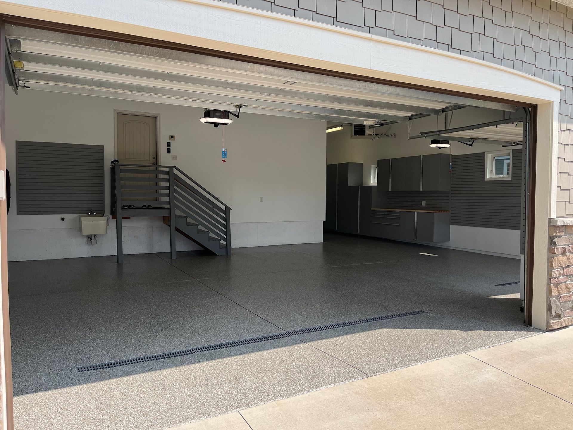 Open garage with tiled floor, stairs, cabinets, and a partially visible car on the right.