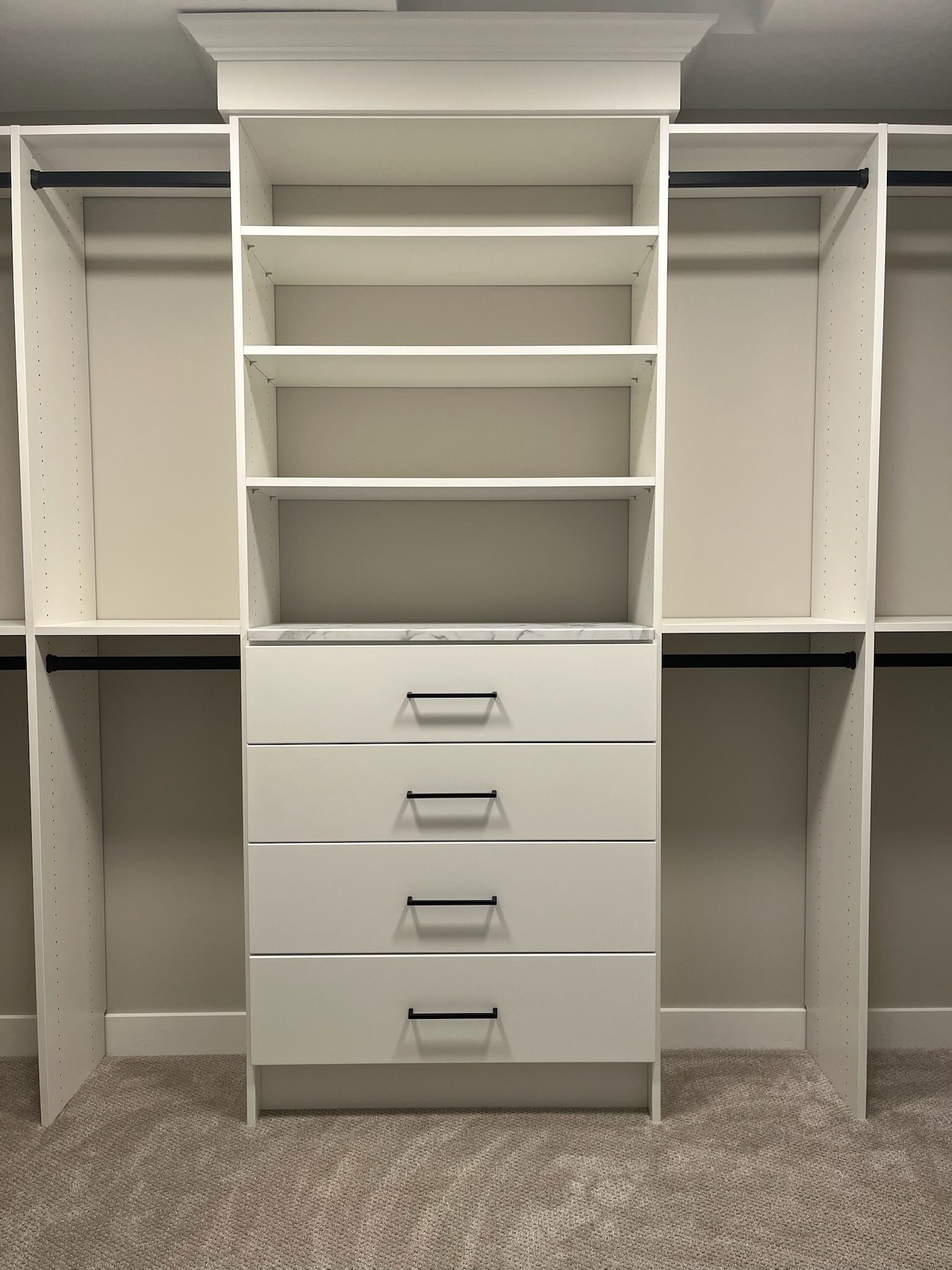 White walk-in closet with shelves, hanging rods, and a central dresser with four drawers.
