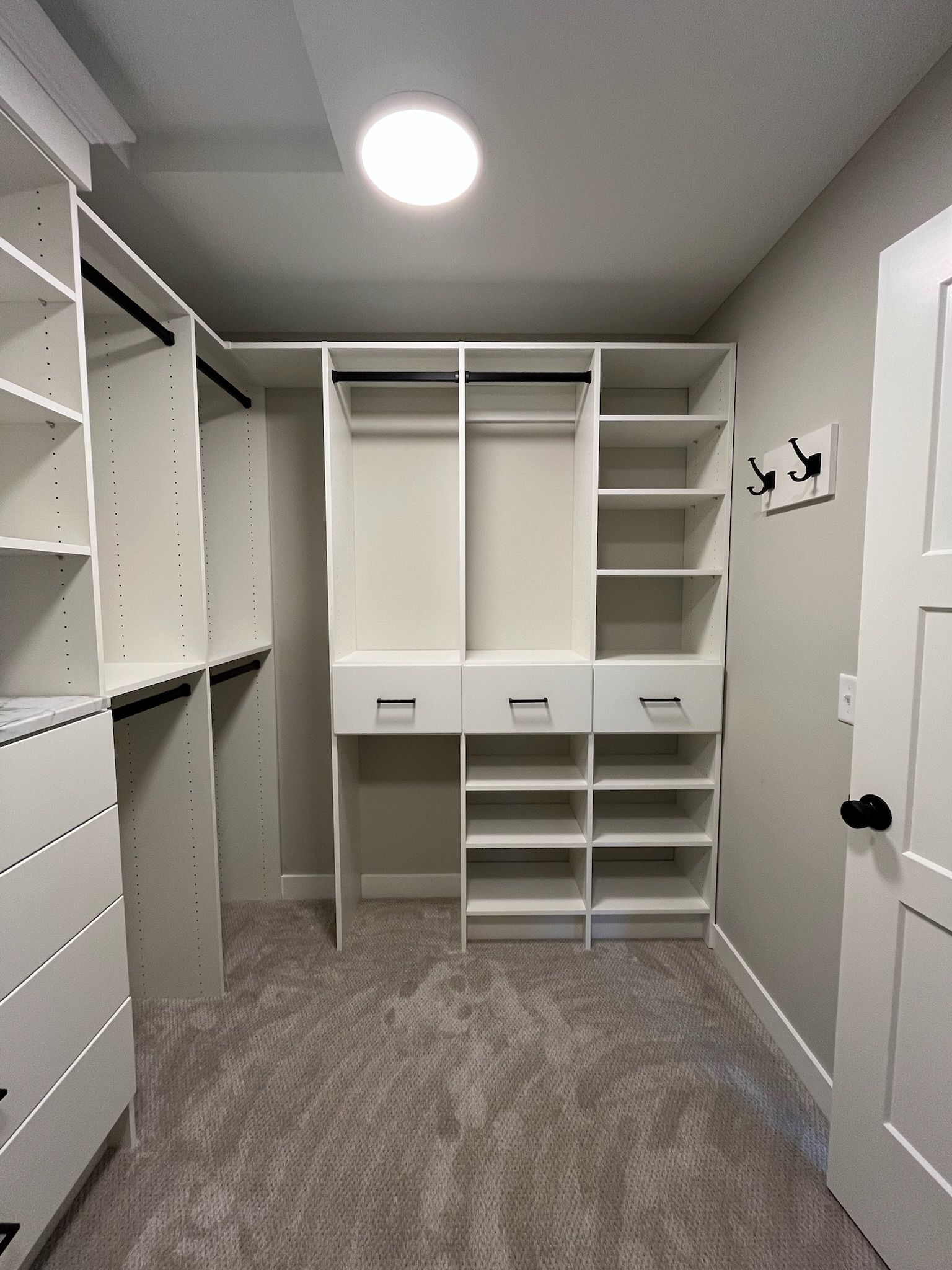 Built-in walk-in closet with white shelving, drawers, and hanging space on gray carpet.