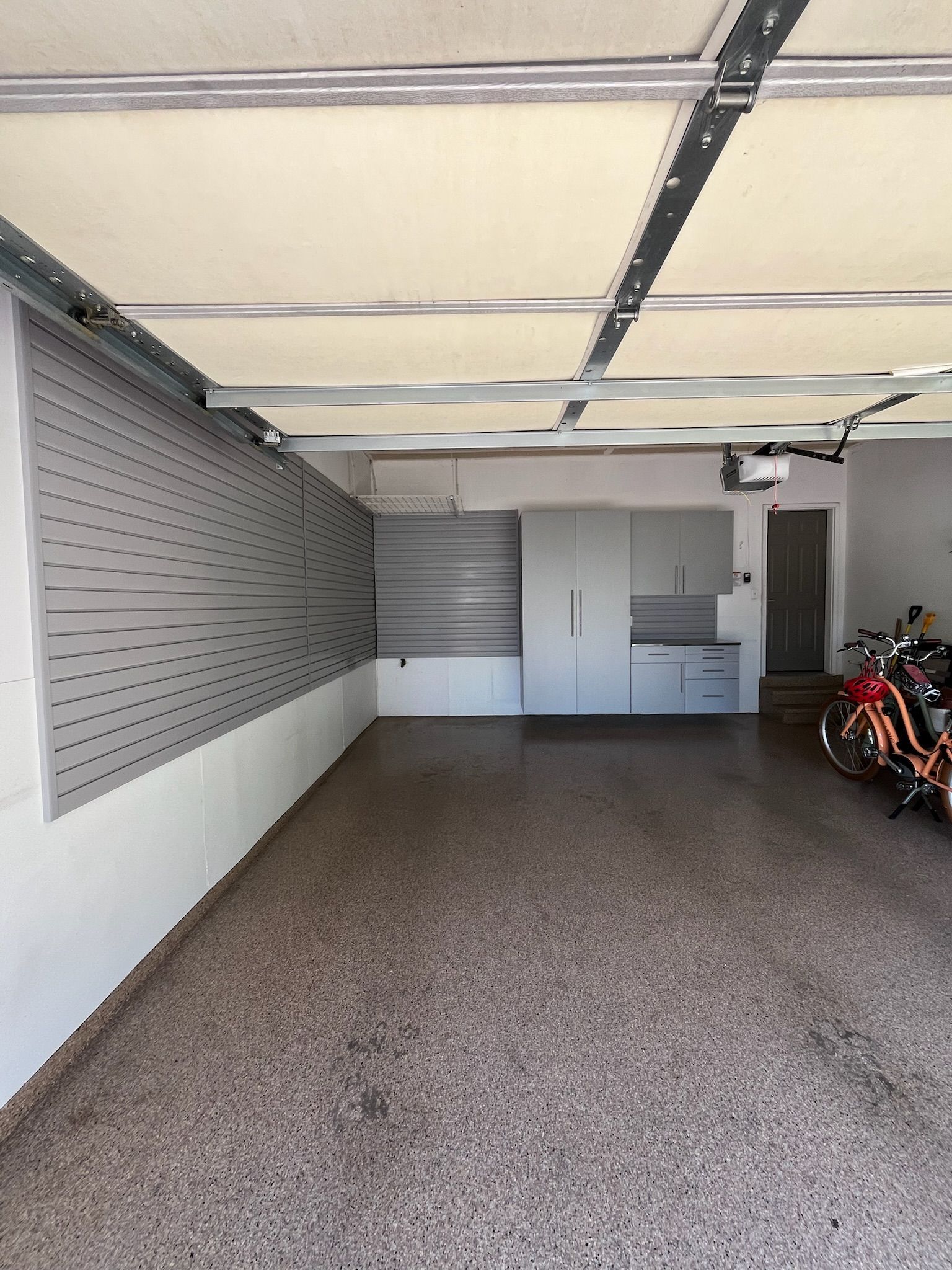 Empty garage with open ceiling, gray walls, storage cabinets, and parked motorcycles along the right side.