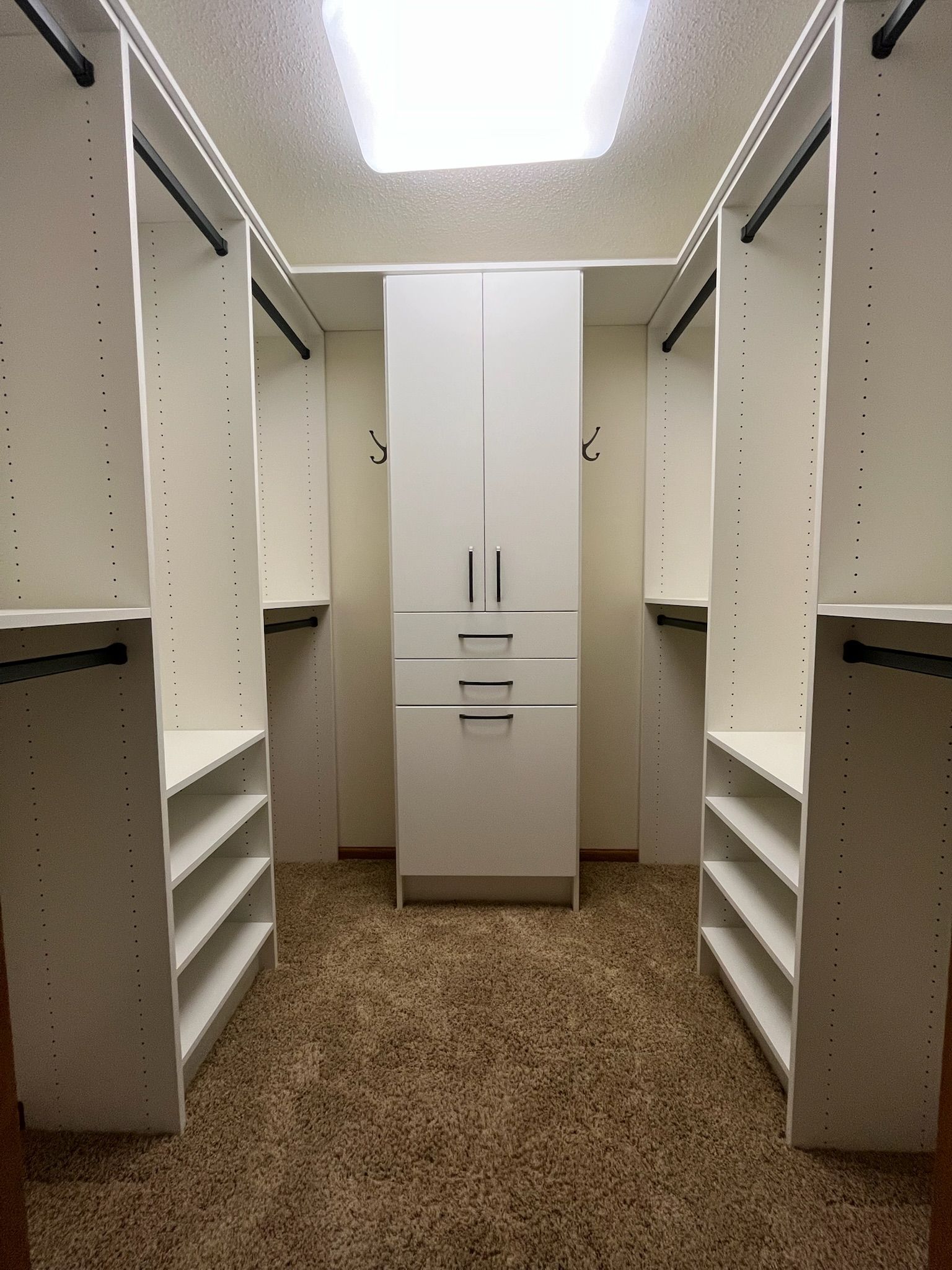 Walk-in closet with white shelving and cabinets on both sides, centered cabinet at the back.