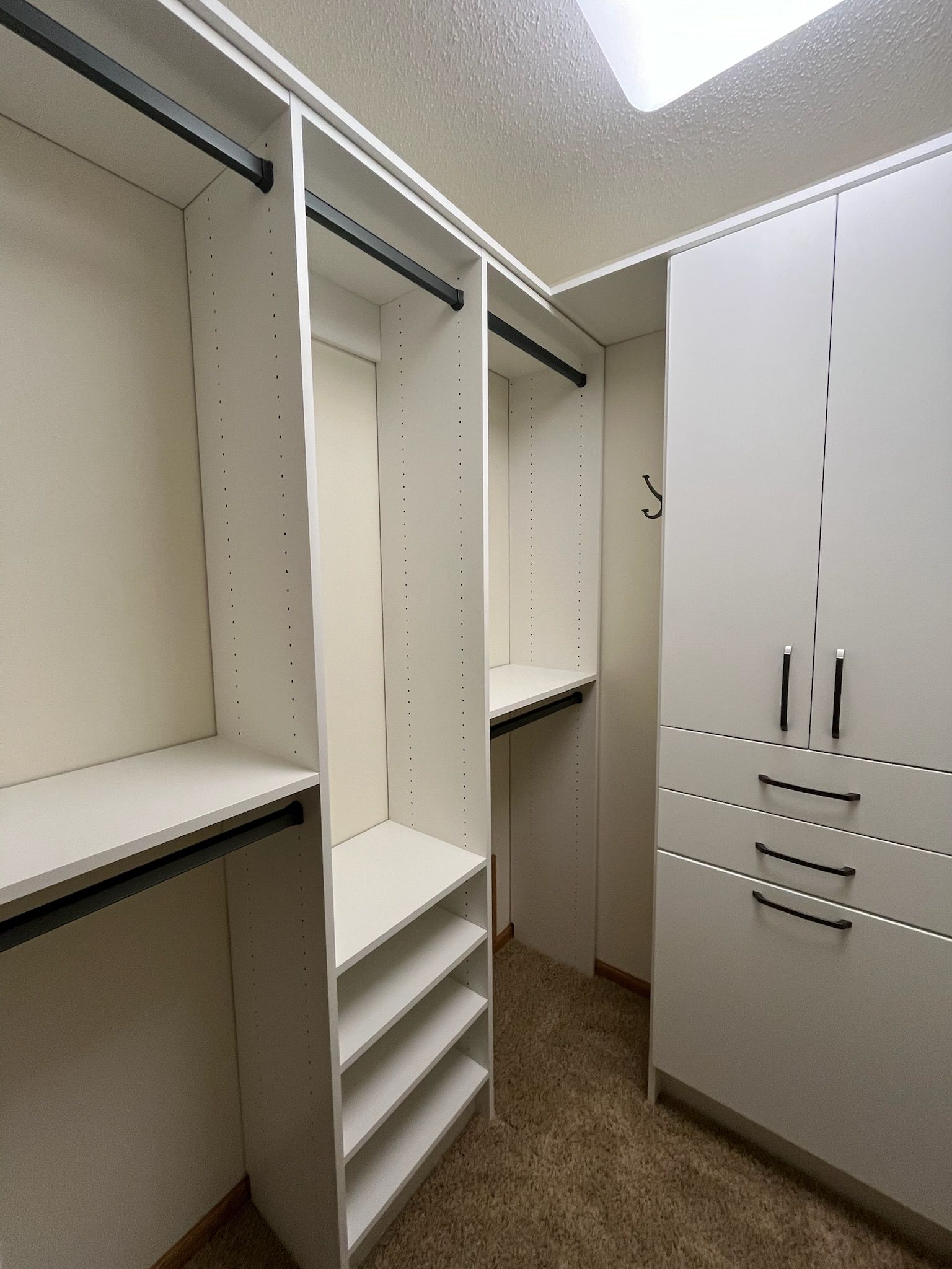 Built-in white closet with shelves, drawers, and hanging rods in a beige carpeted room