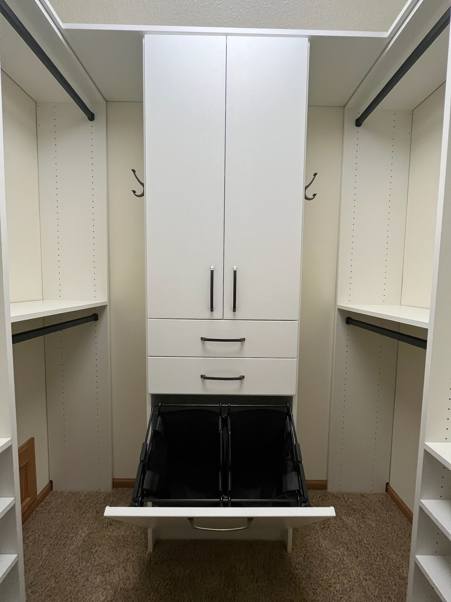 Walk-in closet with white cabinets, shelves, and a central hamper or laundry bin.