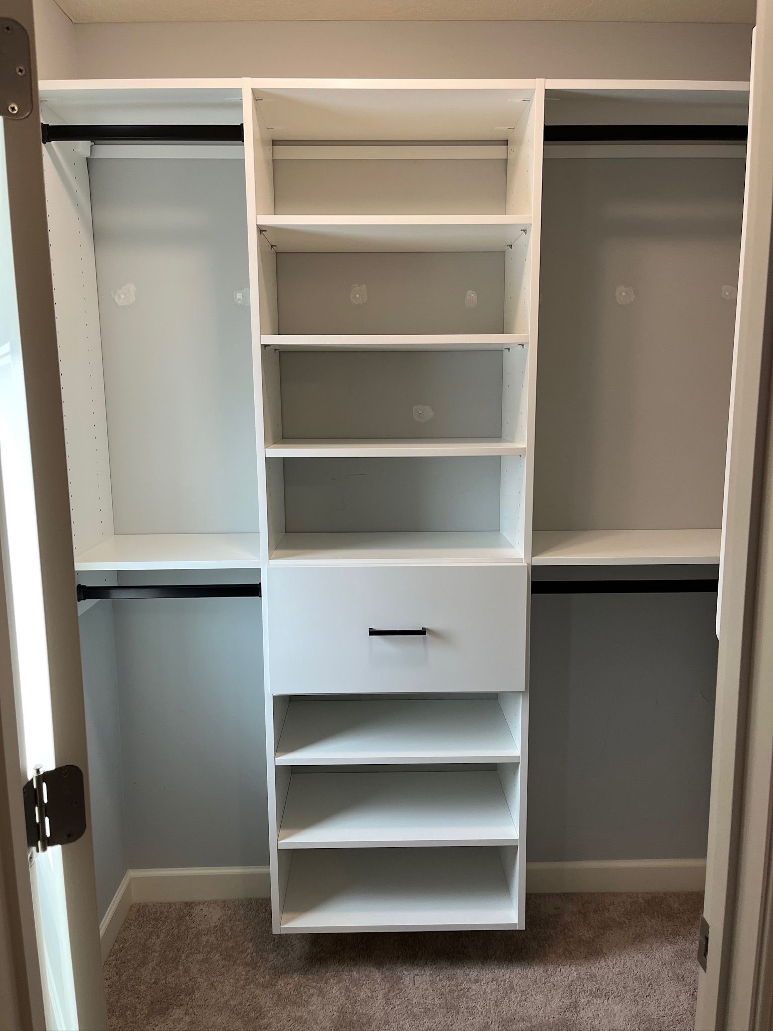 White built-in closet organizer with shelves, drawers, and hanging spaces in an empty closet.