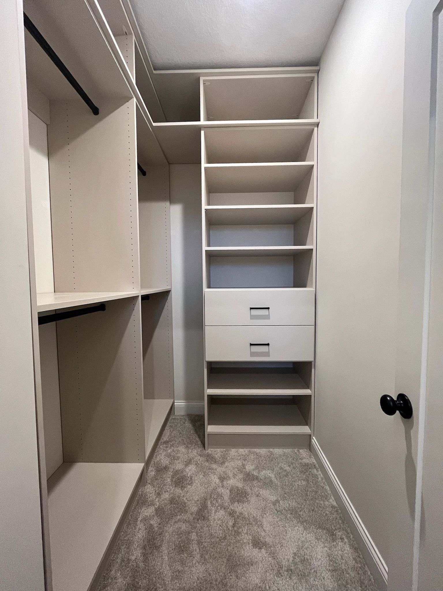 Empty walk-in closet with white shelves, drawers, and a gray carpet.