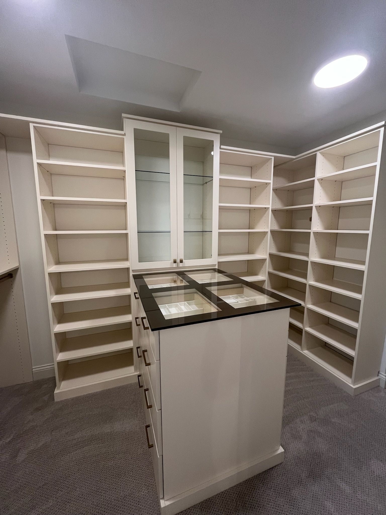 Empty walk-in closet with white shelving and a central island cabinet under recessed lighting.