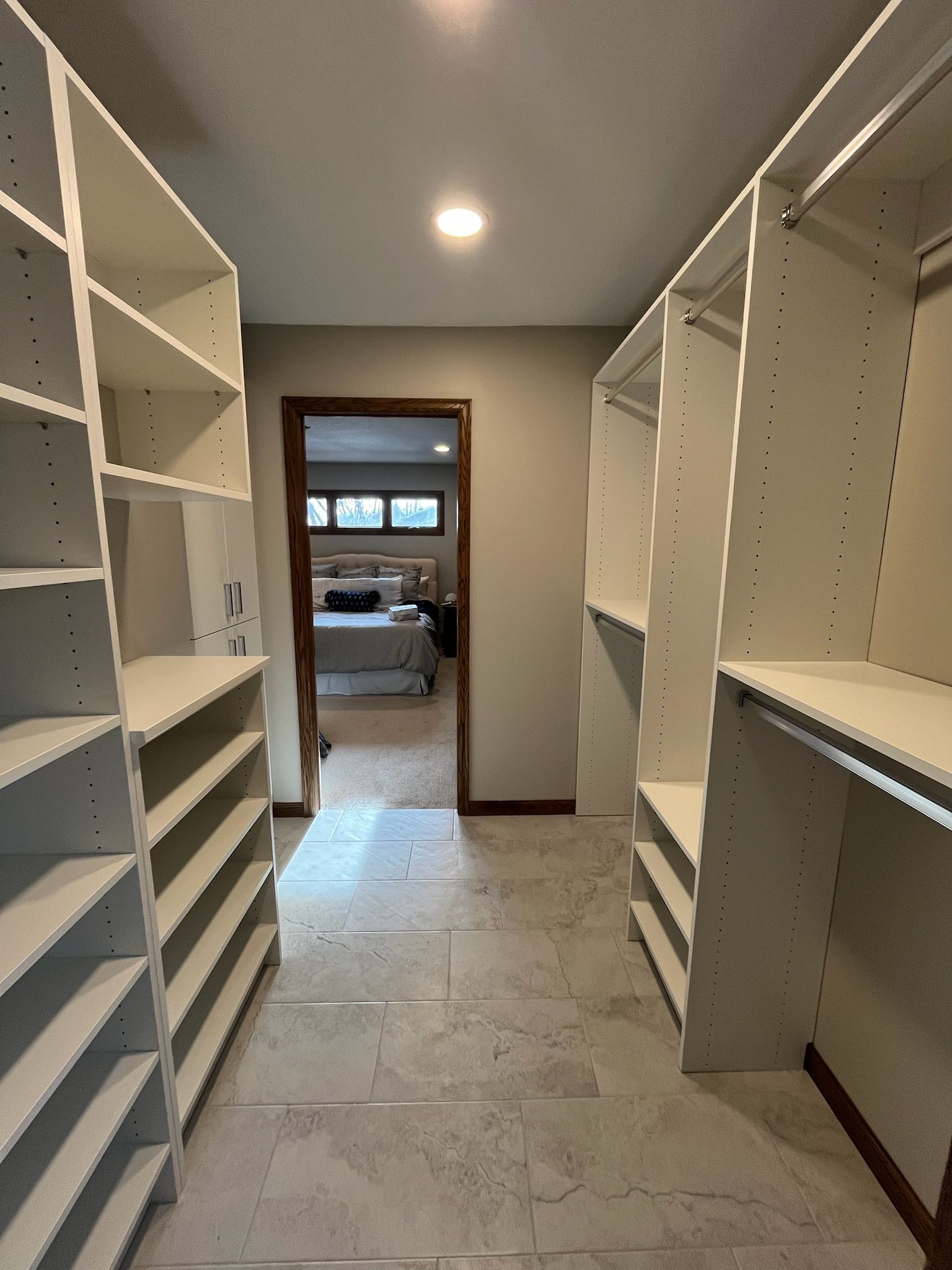 Walk-in closet with white shelving on both sides, leading to a bedroom through an open doorway.