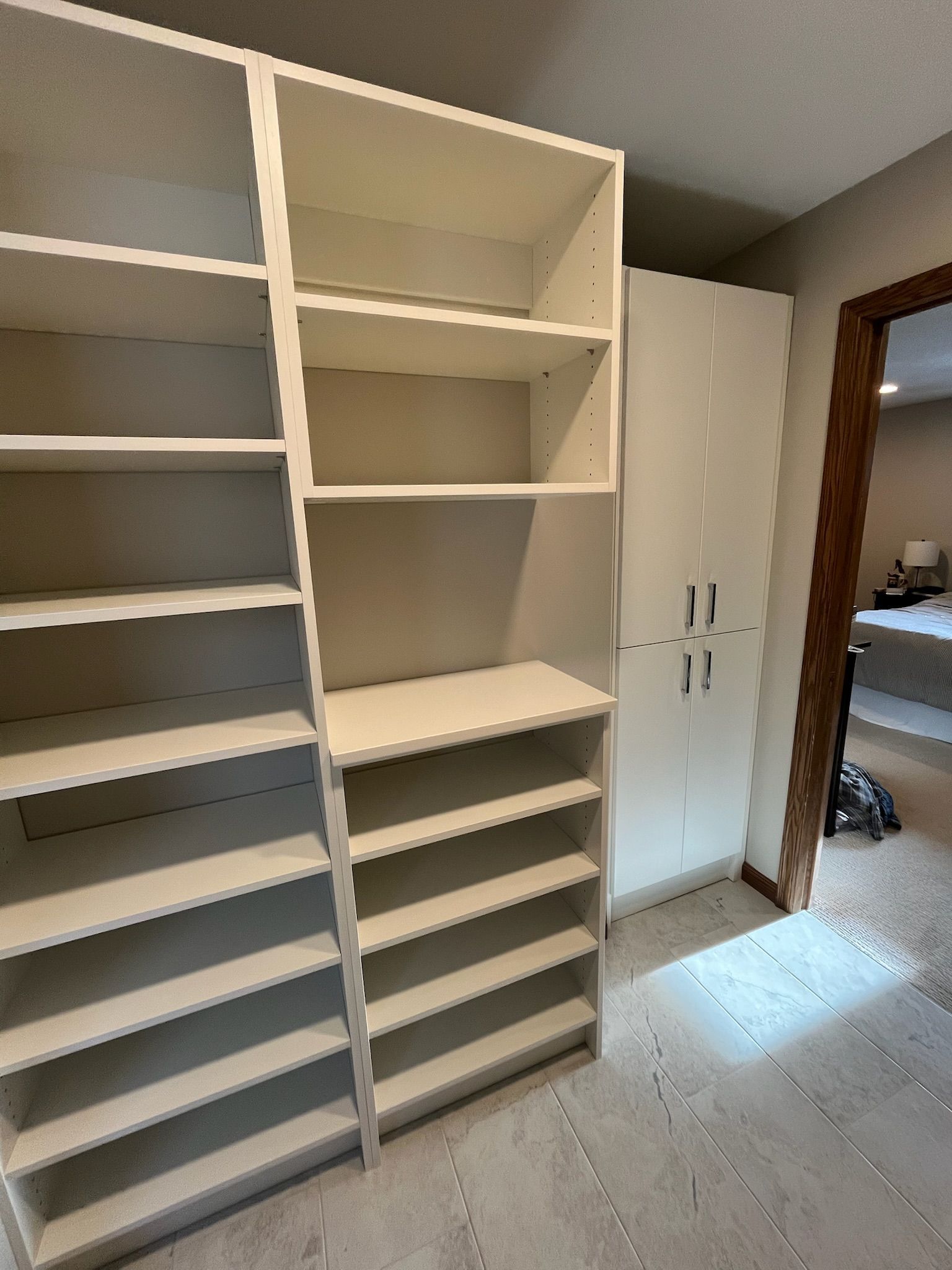 Built-in white closet shelves and drawers in a bright room with open cabinets and a window.