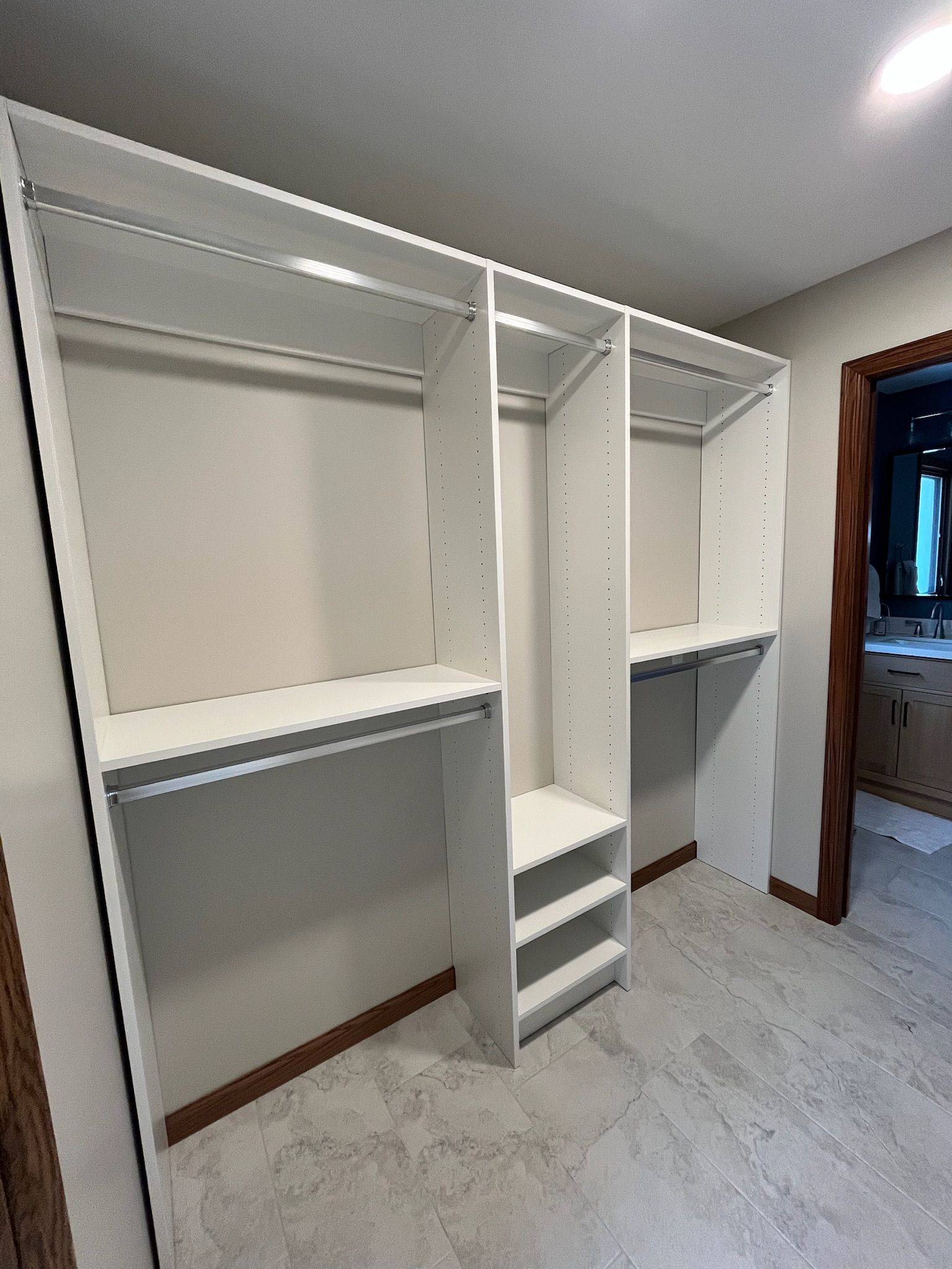 White walk-in closet with built-in shelves, hanging rods, and a central drawer unit in a carpeted room