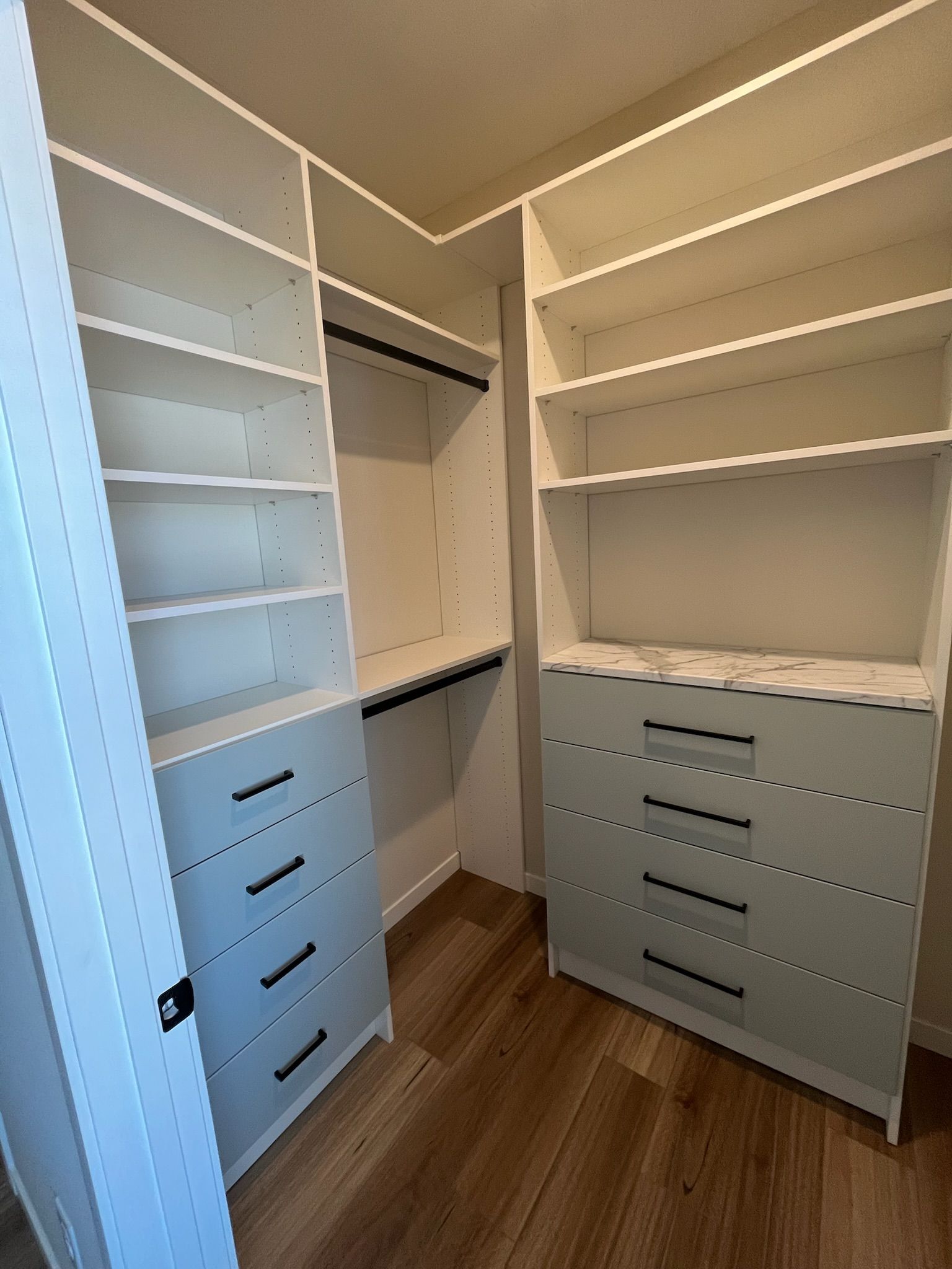 Custom walk-in closet with white shelves, gray drawers, and wood flooring.