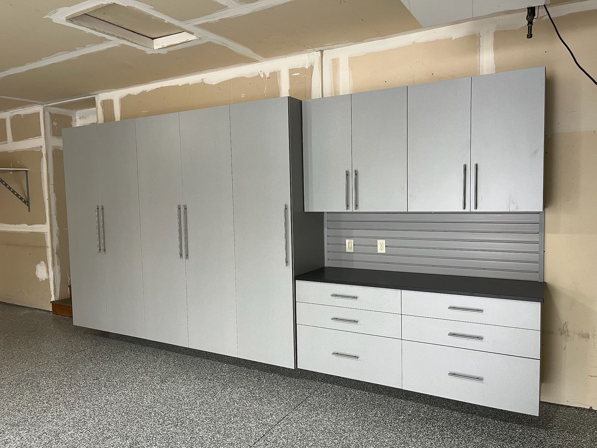 Gray storage cabinets and white drawers along a garage wall with a black countertop and pegboard backsplash.