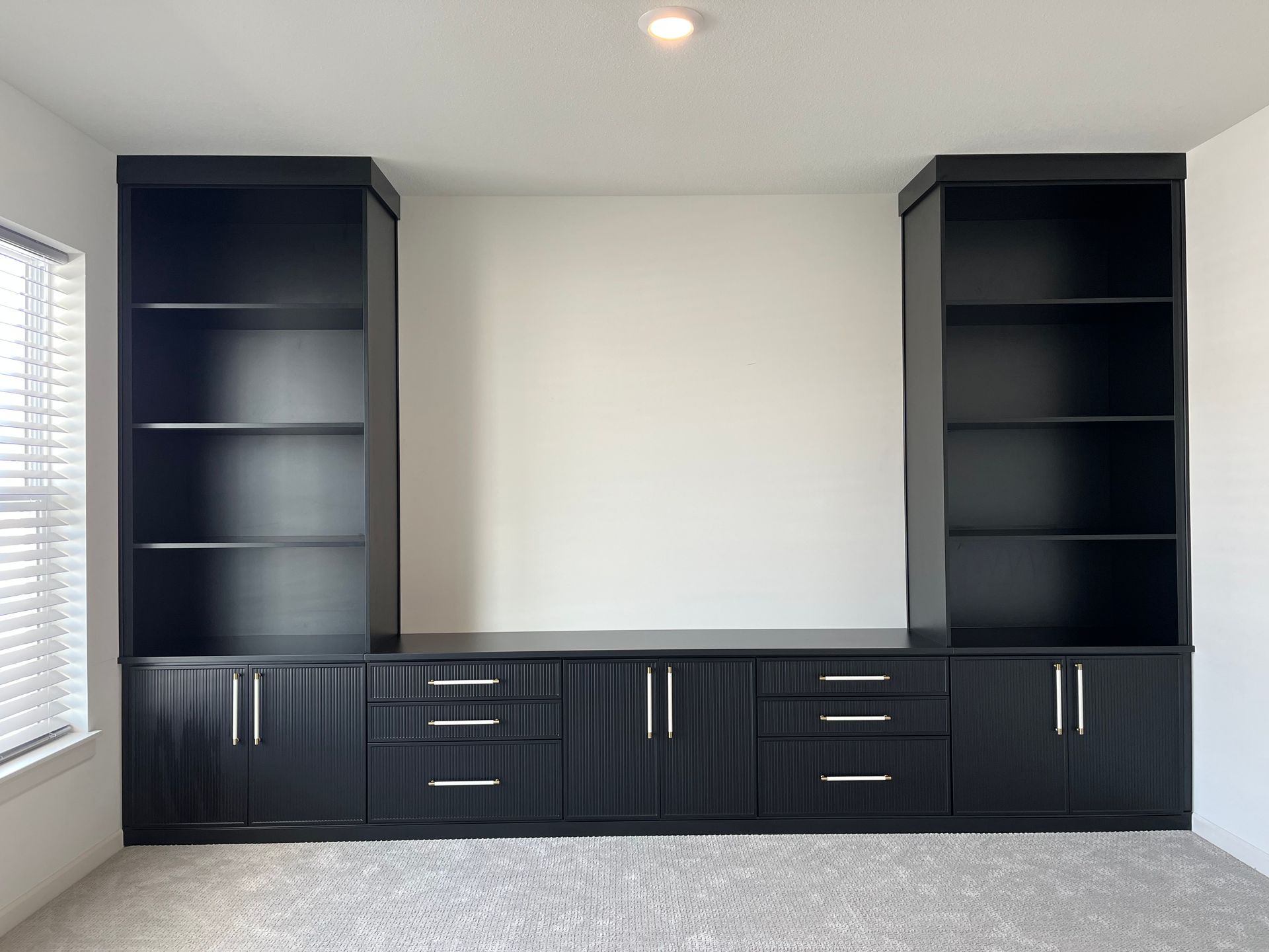 Black built-in cabinets and bookshelves along a wall in a bright empty room