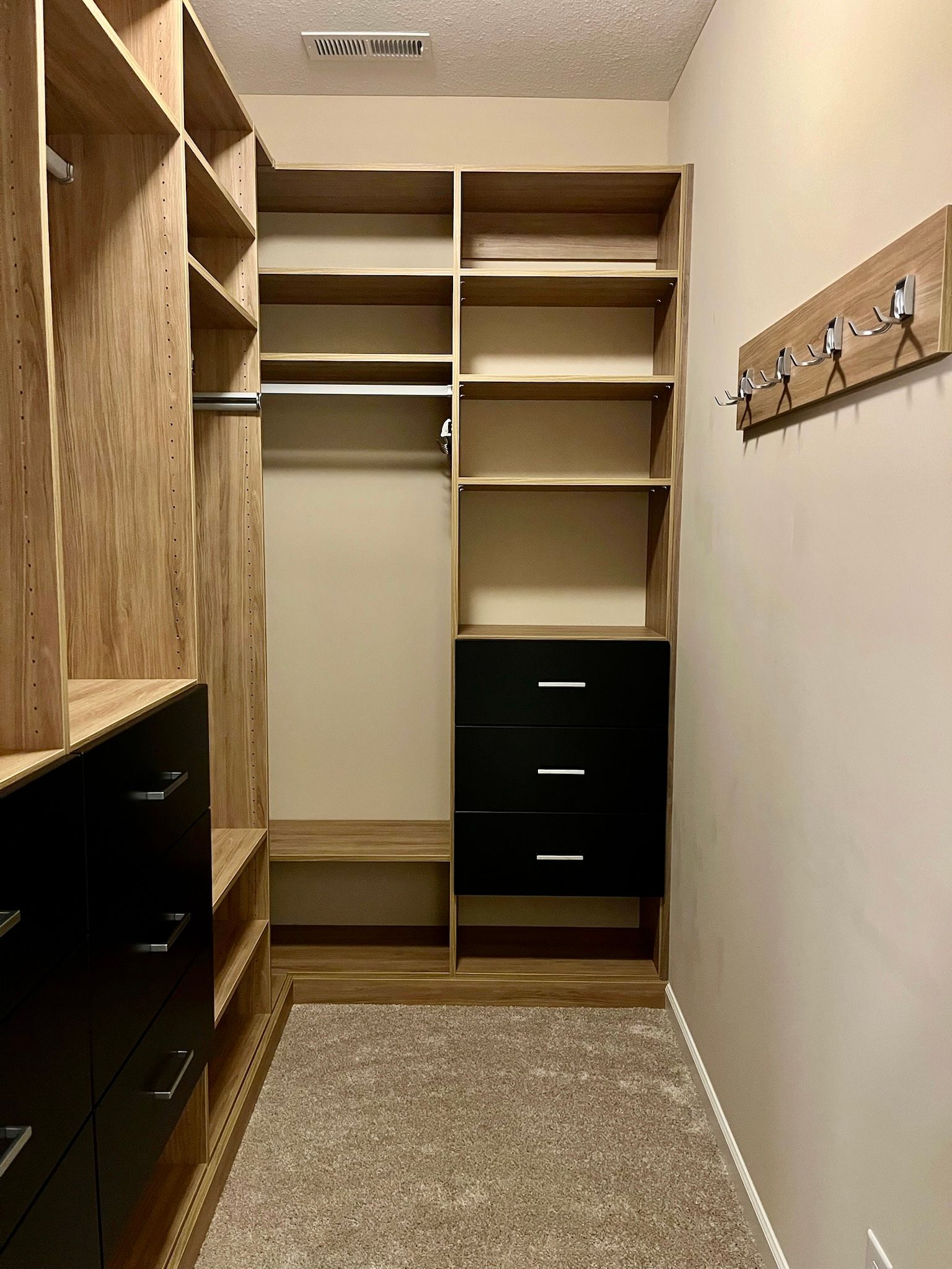 Empty walk-in closet with wooden shelves, black drawers, and a carpeted floor.