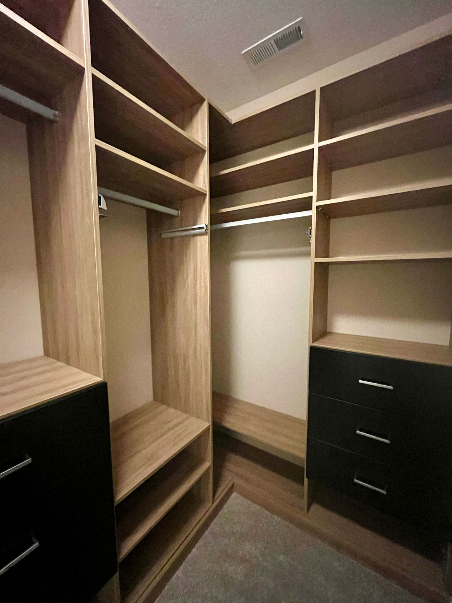 Empty walk-in closet with wood shelves, hanging rods, and dark drawers on the right
