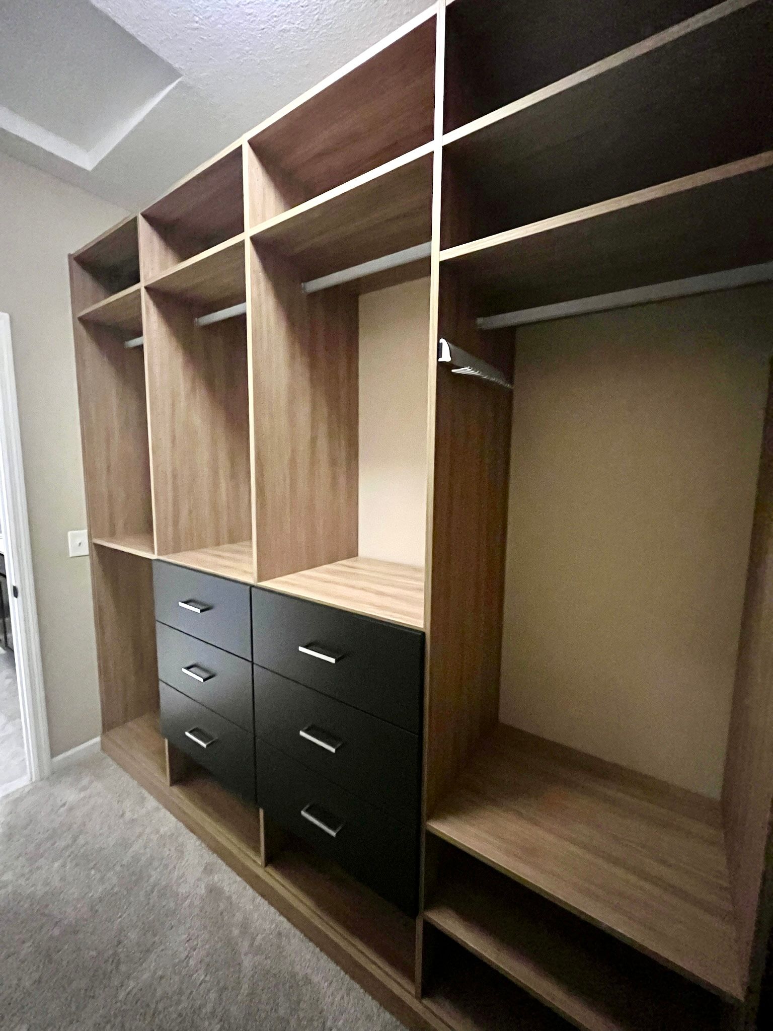 Built-in closet organizers with wooden shelving and black drawers in a carpeted room.