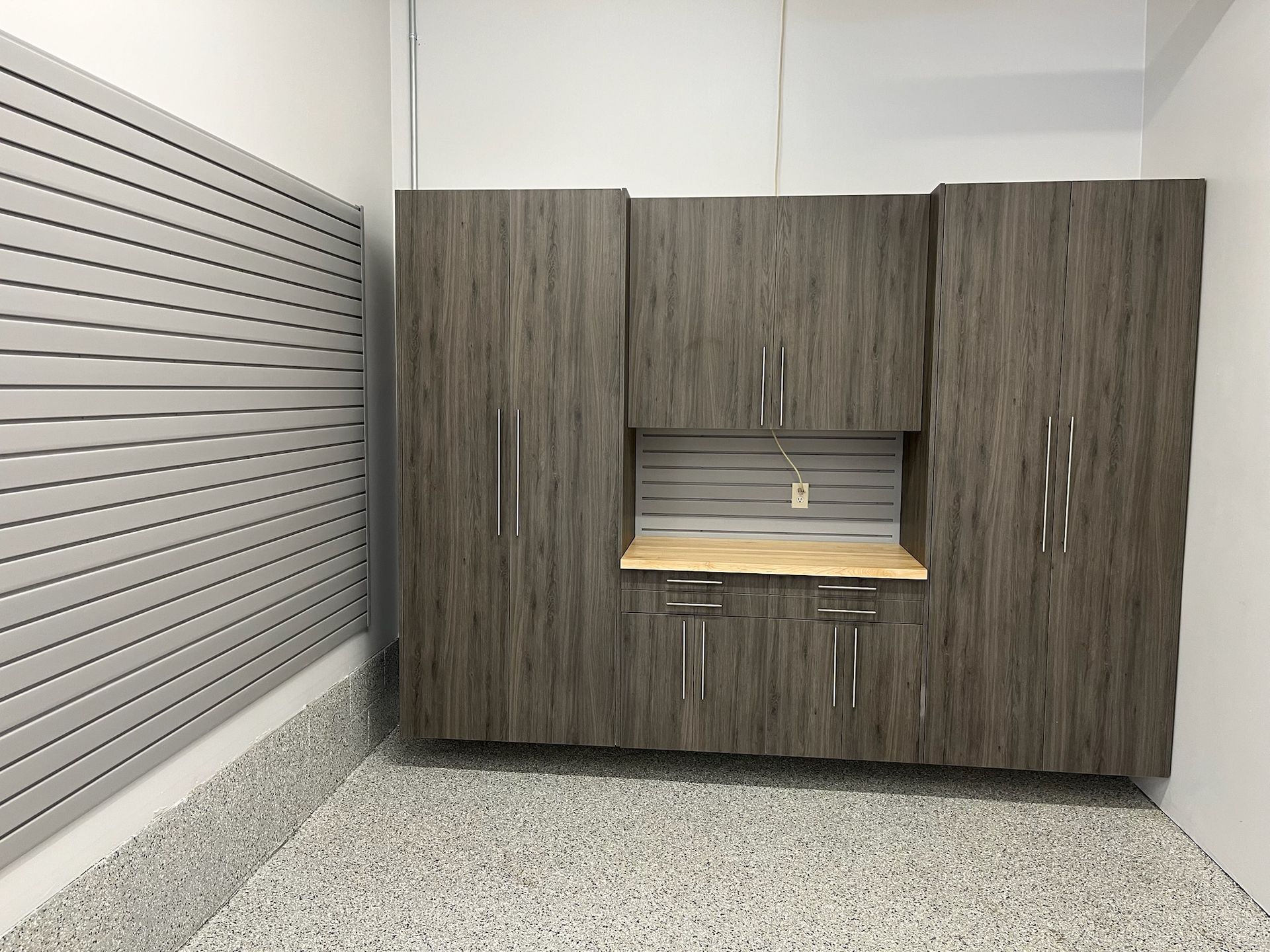 Small office storage cabinet with wood grain doors and a central countertop in a white-walled room