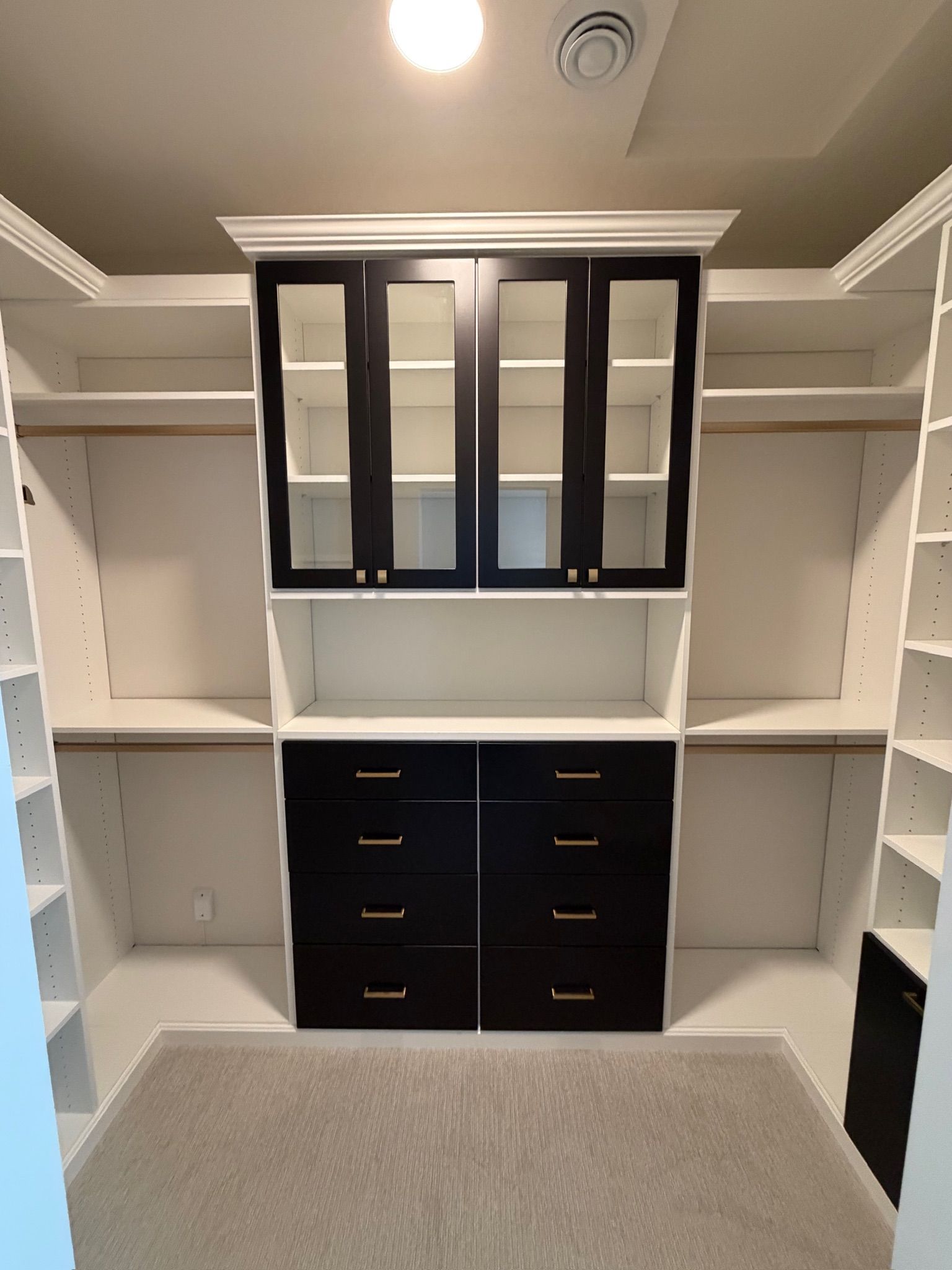 Walk-in closet with white shelving, black drawers, and black glass-front cabinets under a ceiling light.