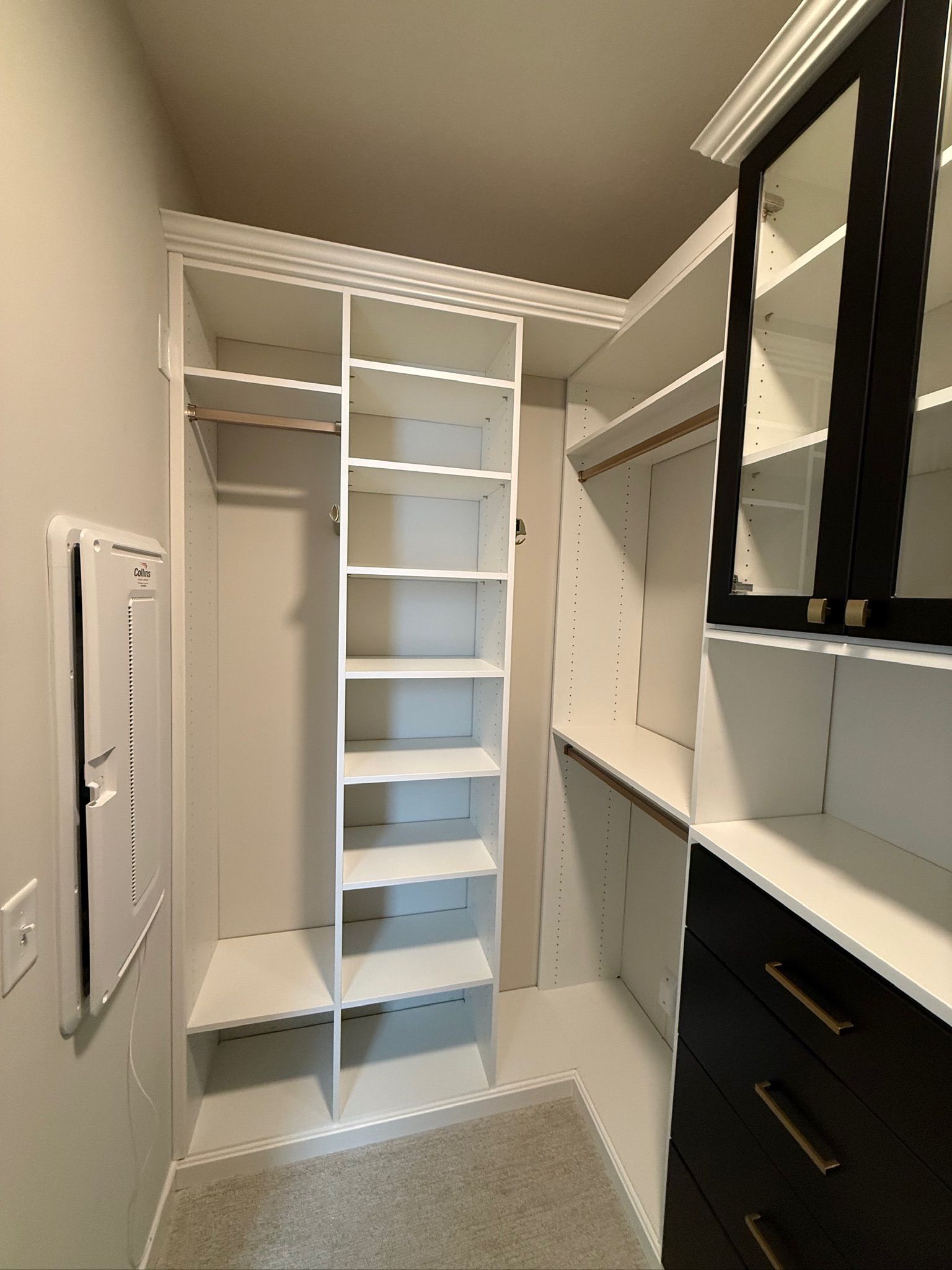 Walk-in closet with white built-in shelves, hanging rods, and dark drawers under sloped ceiling.