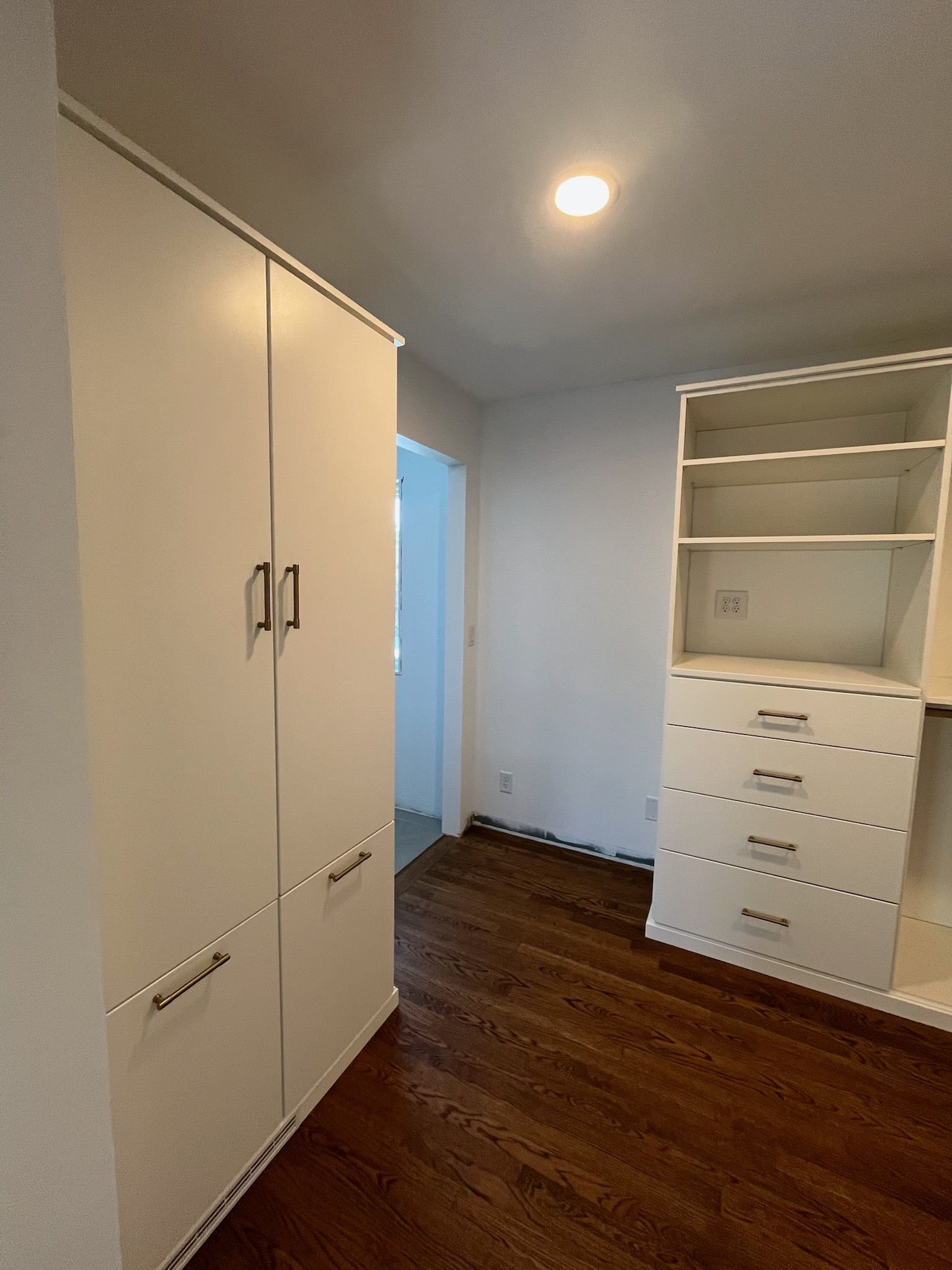 Empty bedroom with white built-in cabinets, wood floor, and an open doorway.