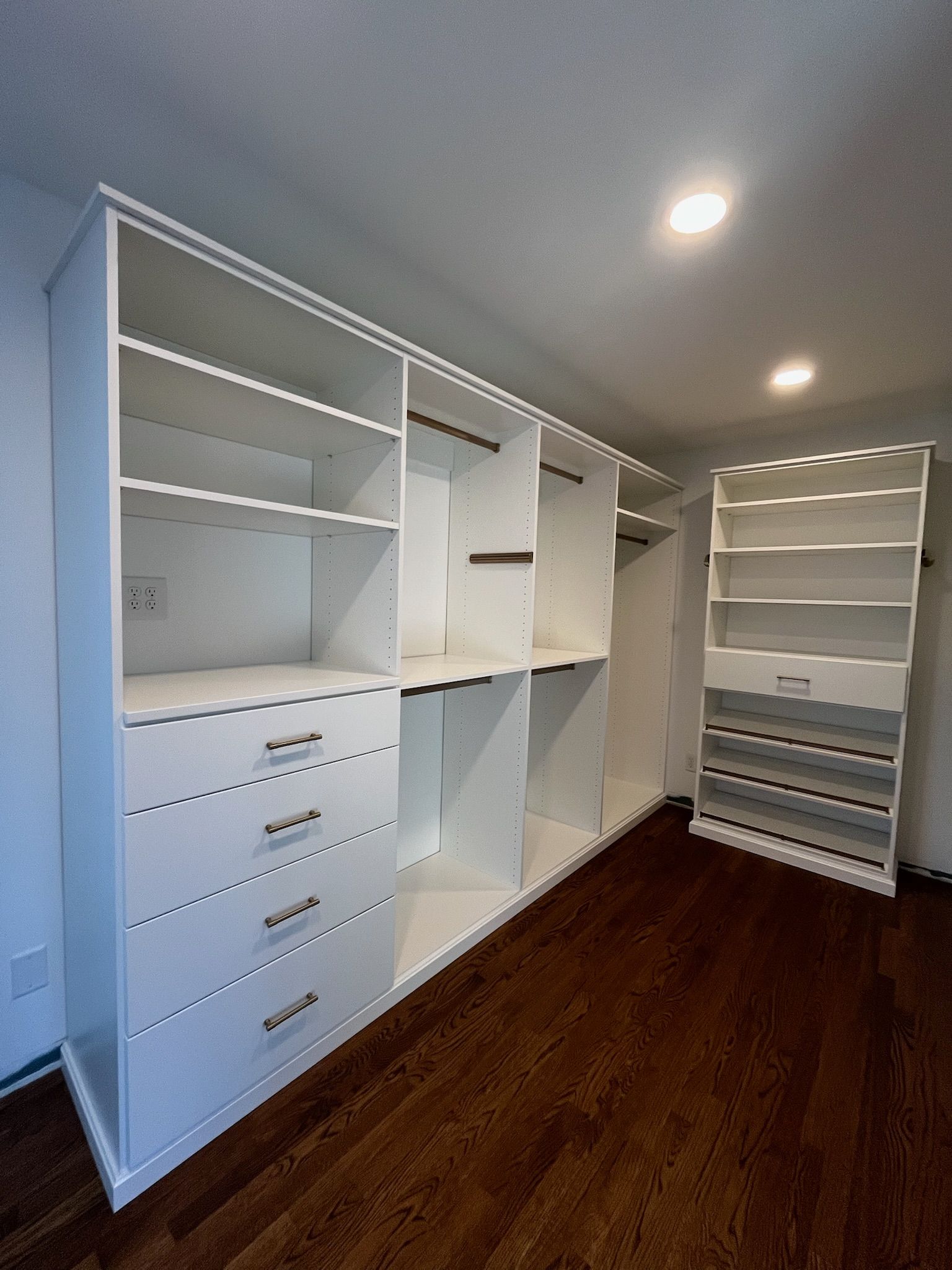 White walk-in closet with built-in shelving, drawers, and hanging space, lit by recessed ceiling lights.