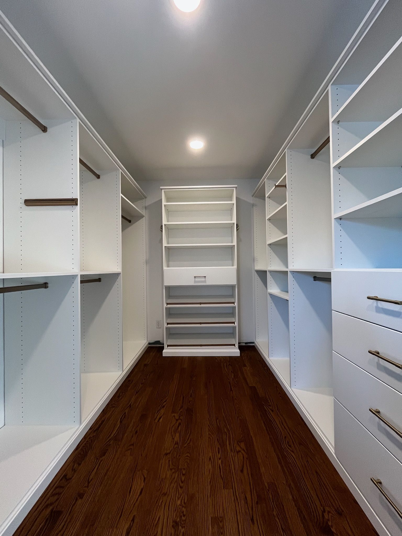 Spacious walk-in closet with white shelving and hanging rods, dark wood floor, and a central shelving unit.