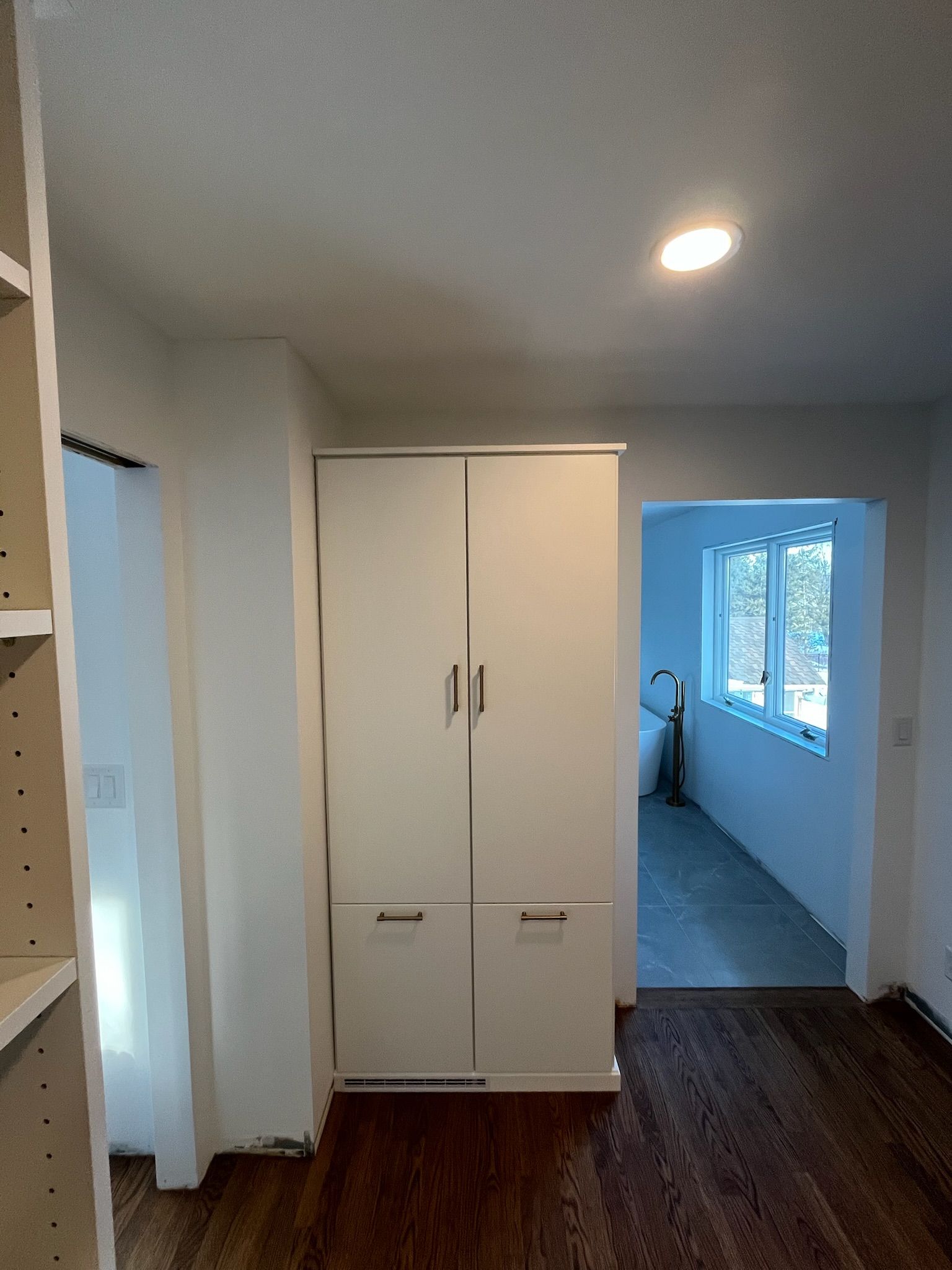 Small room with white wardrobe, wood floor, recessed light, and hallway with windows.