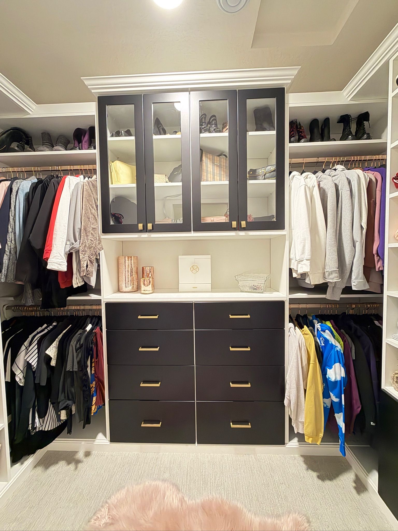 Built-in closet with dark drawers, glass cabinets, hanging clothes, and shoes on upper shelves